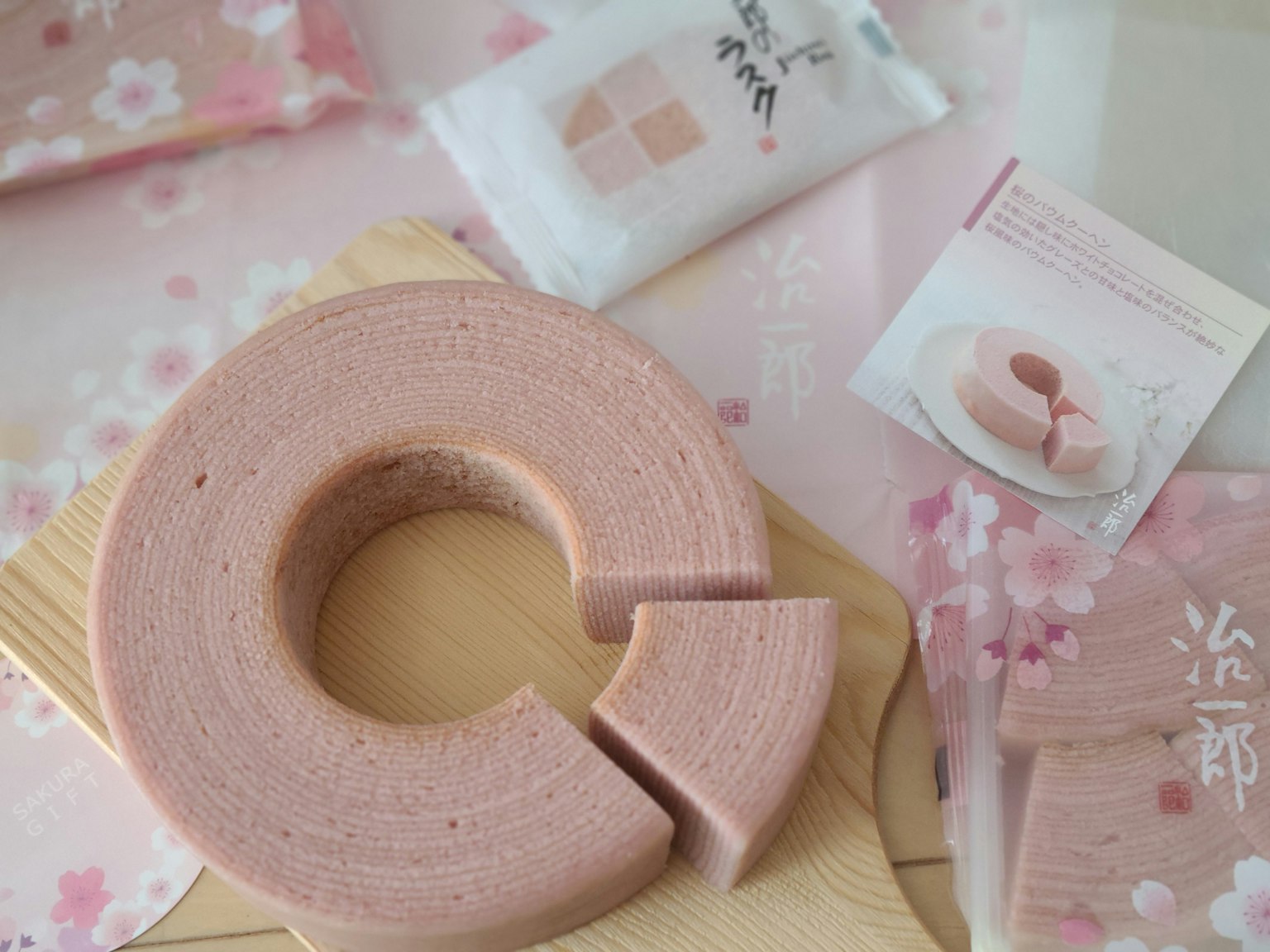 Baumkuchen de color sakura colocado sobre un plato de madera con empaques y una tarjeta cercana