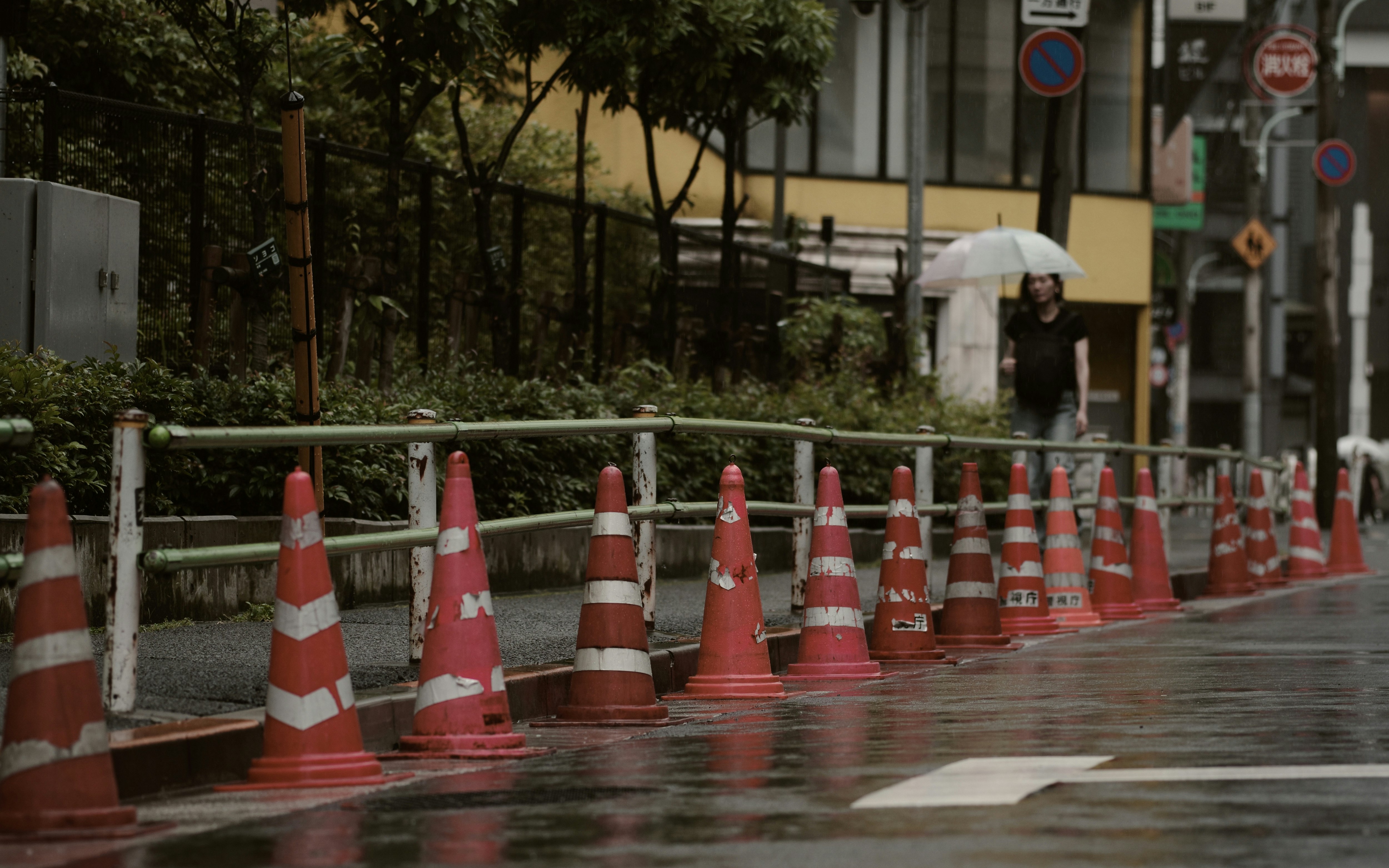 雨上がりの路上に並ぶコーンと歩行者のある街角