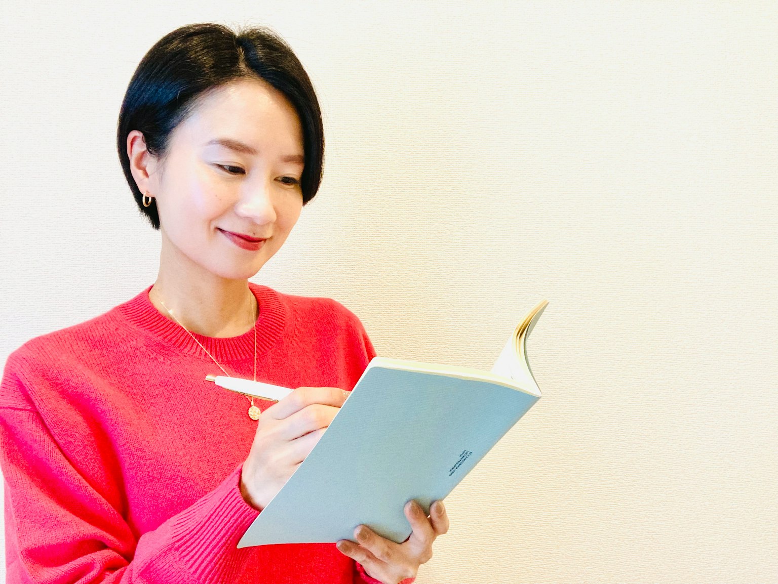 女性穿着亮粉色毛衣在笔记本上写字