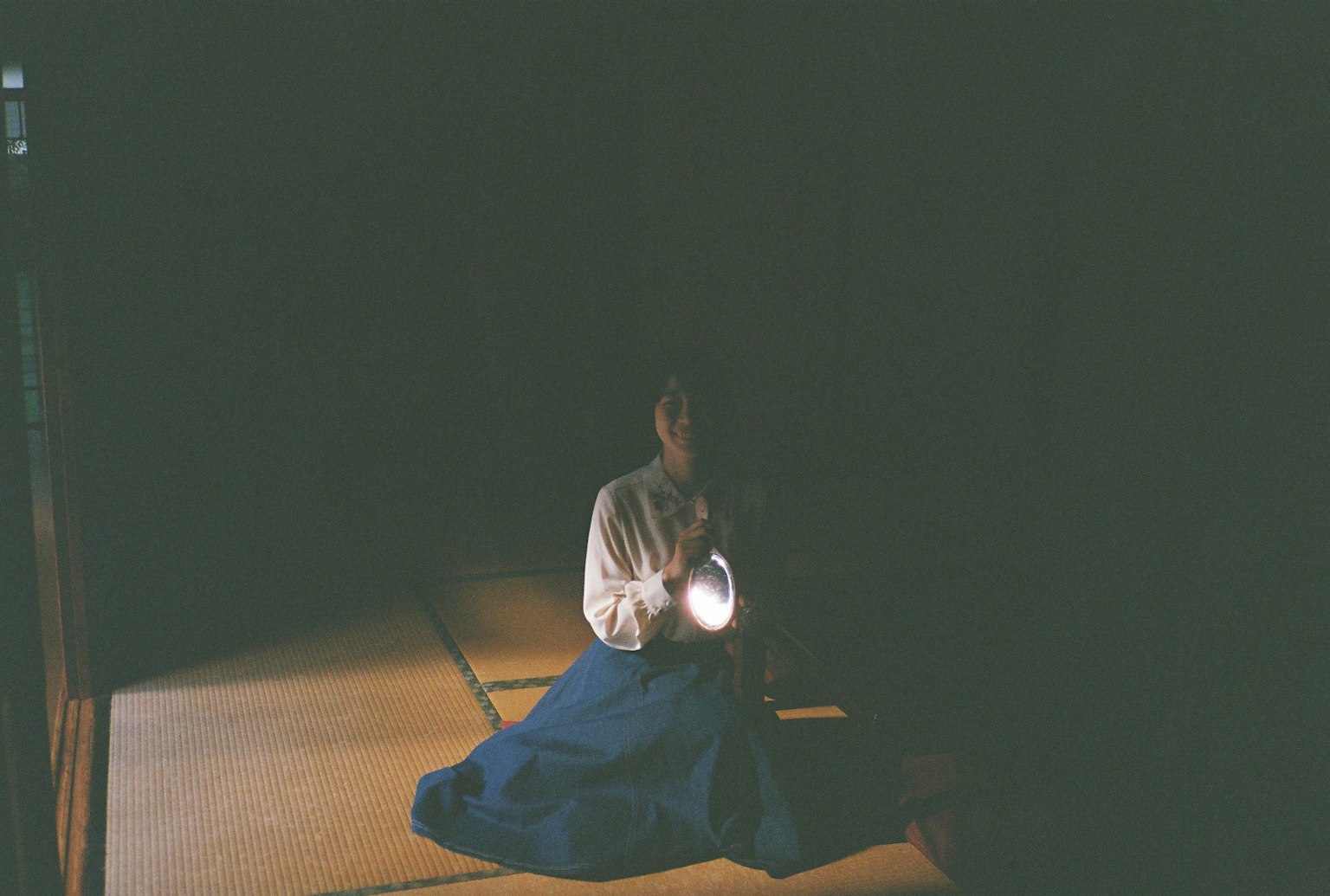 暗い部屋で懐中電灯を持つ女性が座っている