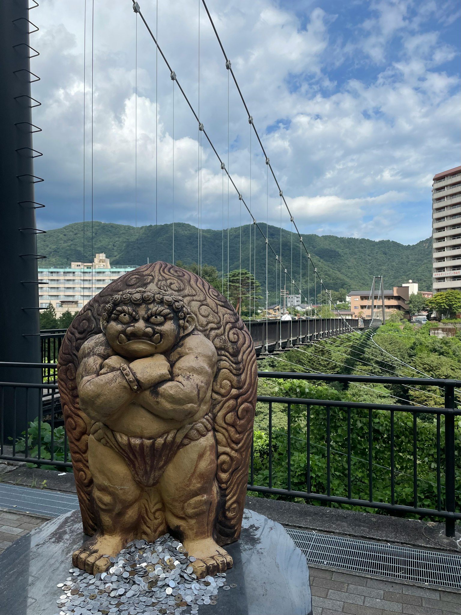 รูปปั้นขนาดใหญ่ของเทพที่อยู่ใกล้สะพานพร้อมภูเขาที่สวยงามในพื้นหลัง