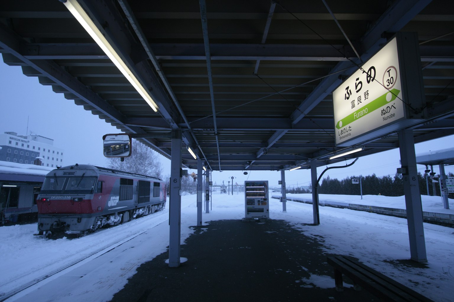 Plateforme de gare enneigée avec un train et des panneaux
