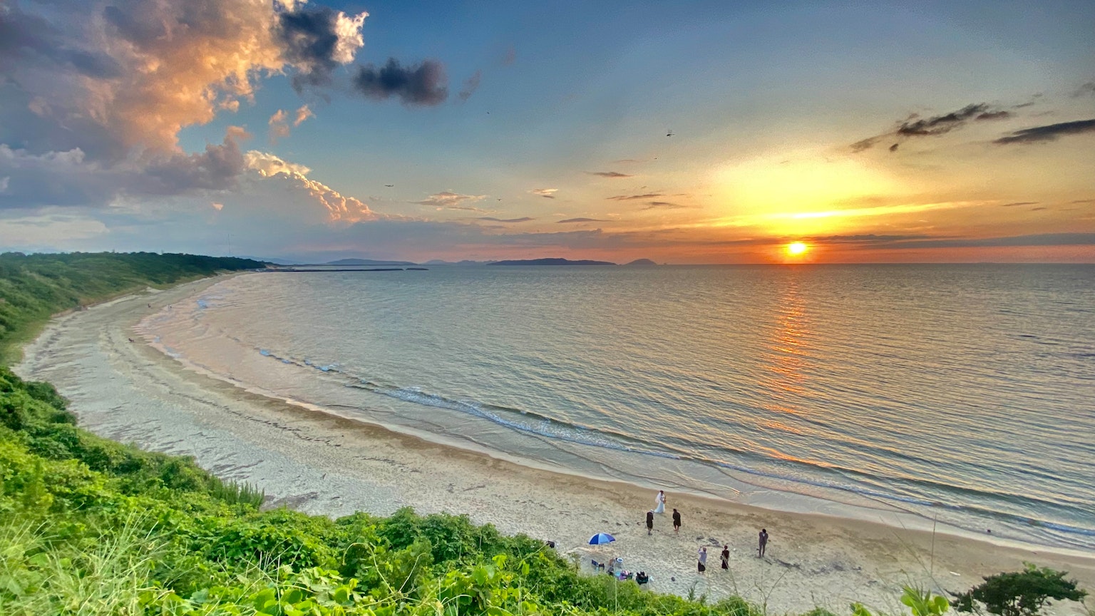 Malersicher Blick auf einen Sonnenuntergang über dem Ozean mit einem Strand und grünem Laub