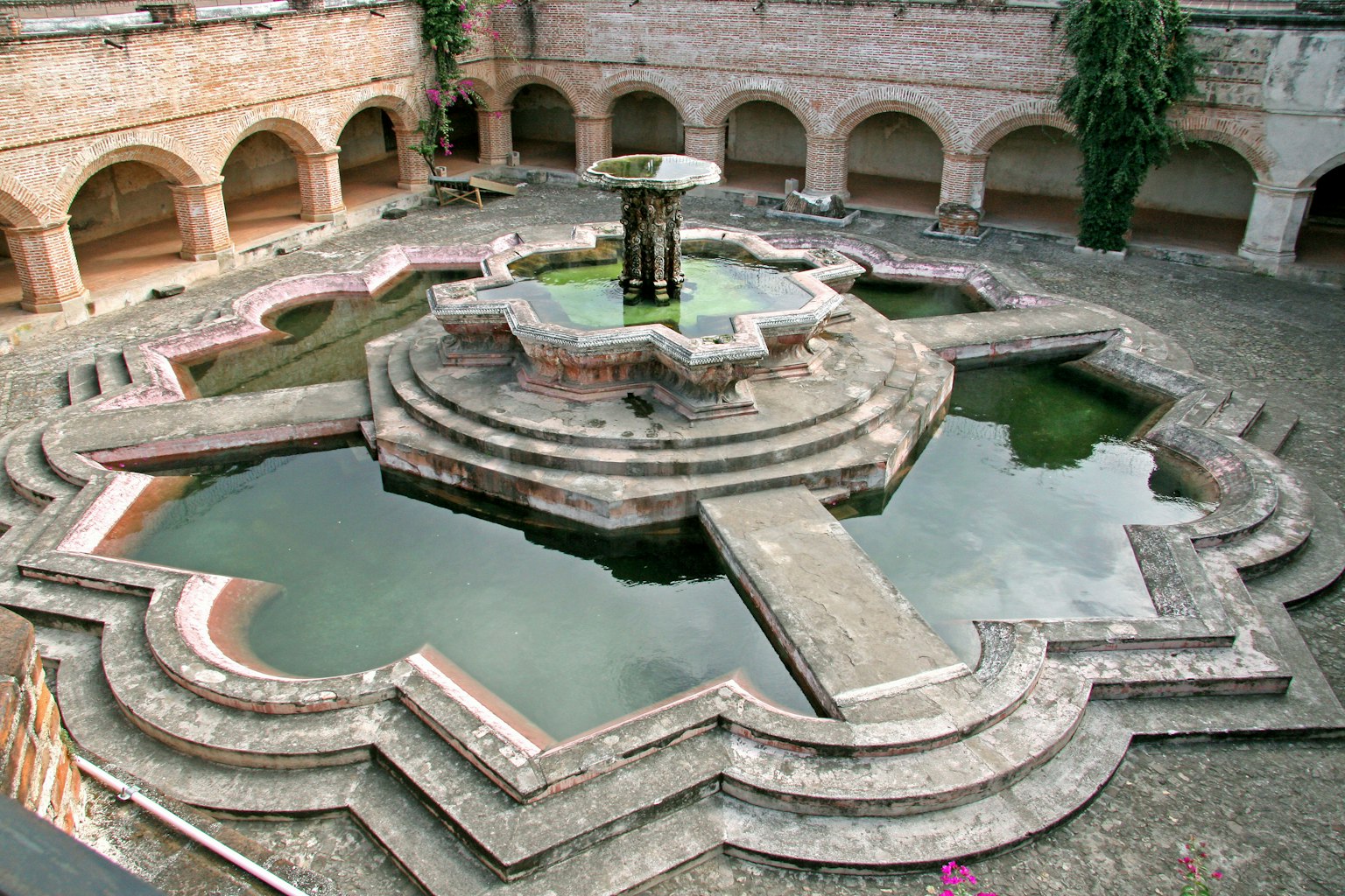 Ein malerischer Innenhof mit einem schönen Steinbrunnen und komplizierten geometrischen Steinrändern mit ruhigem grünem Wasser