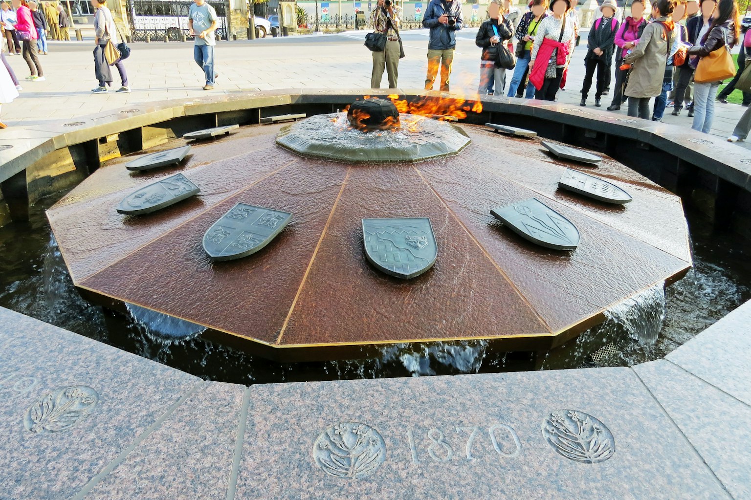Achtkantiger Brunnen mit brennender Flamme und umstehenden Touristen