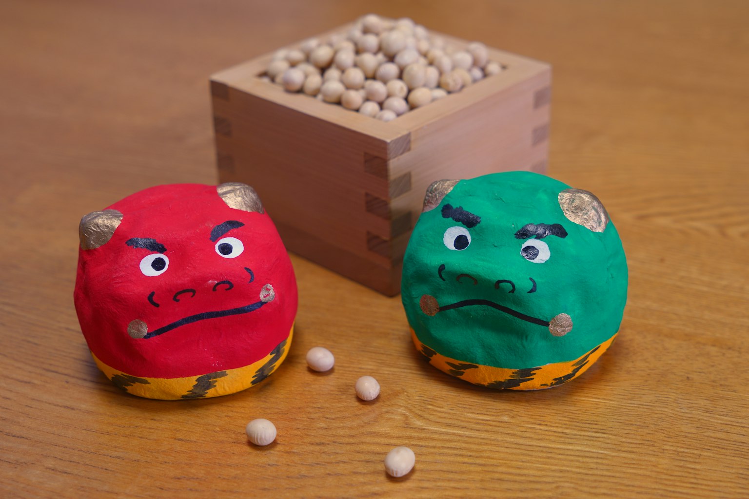 Personajes de demonios de arcilla roja y verde con una caja de madera de frijoles al fondo