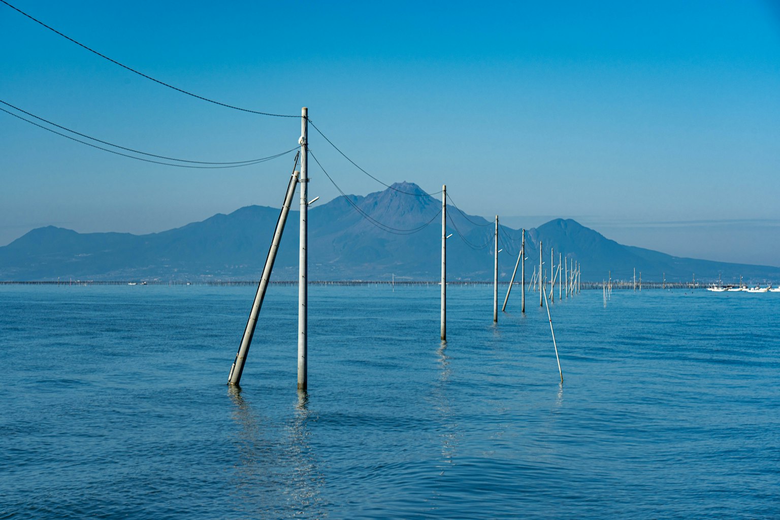 Row of utility poles in the blue water with mountains in the background