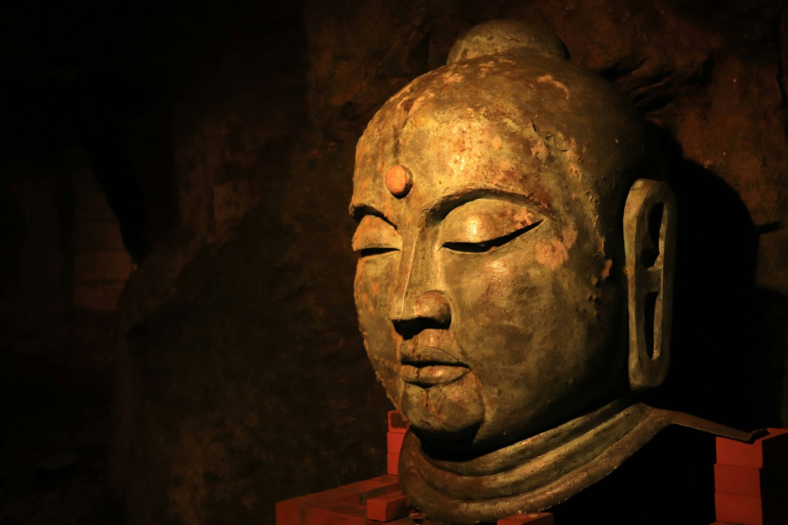 Kepala patung Buddha kuno di gua gelap yang diterangi cahaya lembut