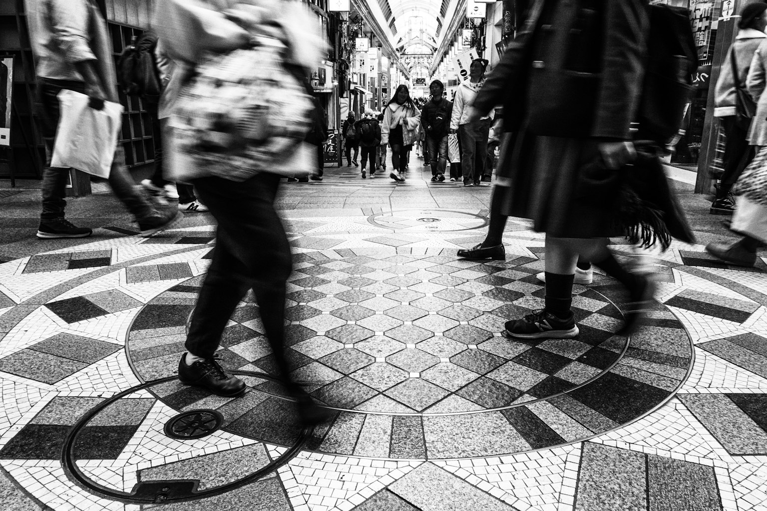 Black and white image of people walking in a shopping arcade with intricate tiled floor
