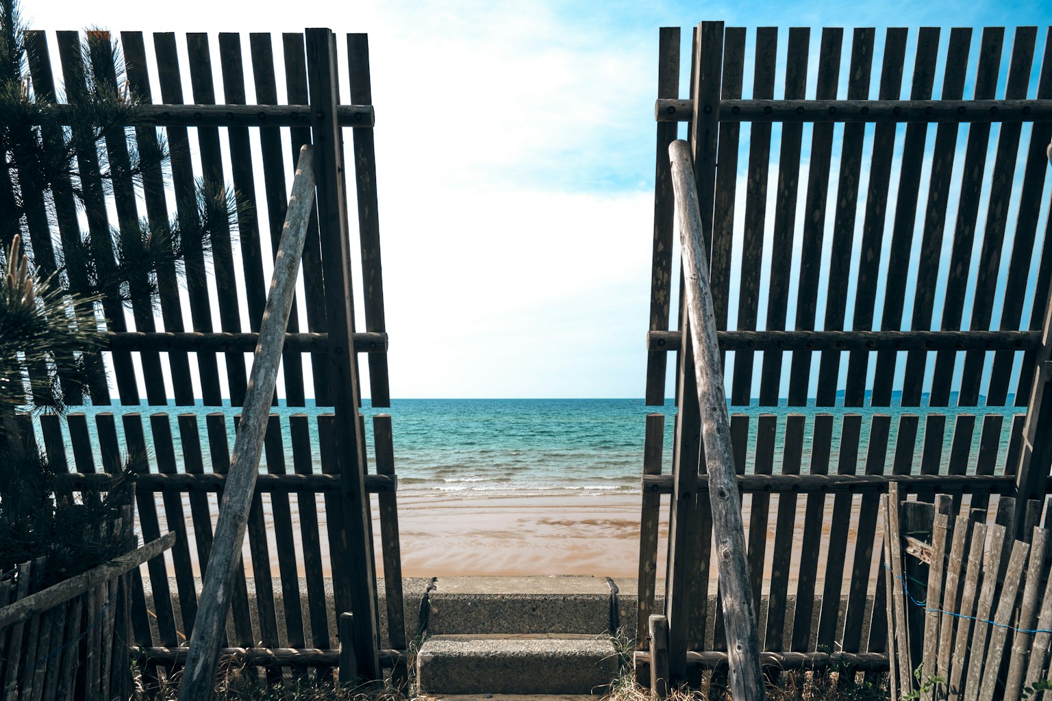 Recinzione in legno che si apre su una spiaggia di sabbia e un oceano blu