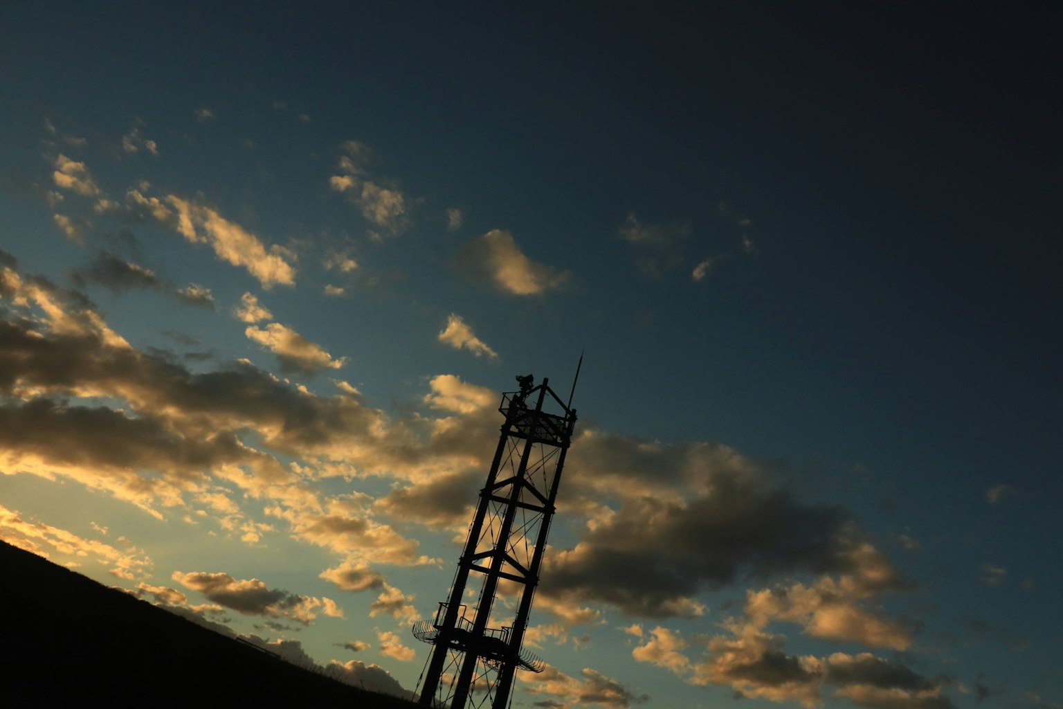 Silhouette di una torre di comunicazione contro un cielo colorato al tramonto