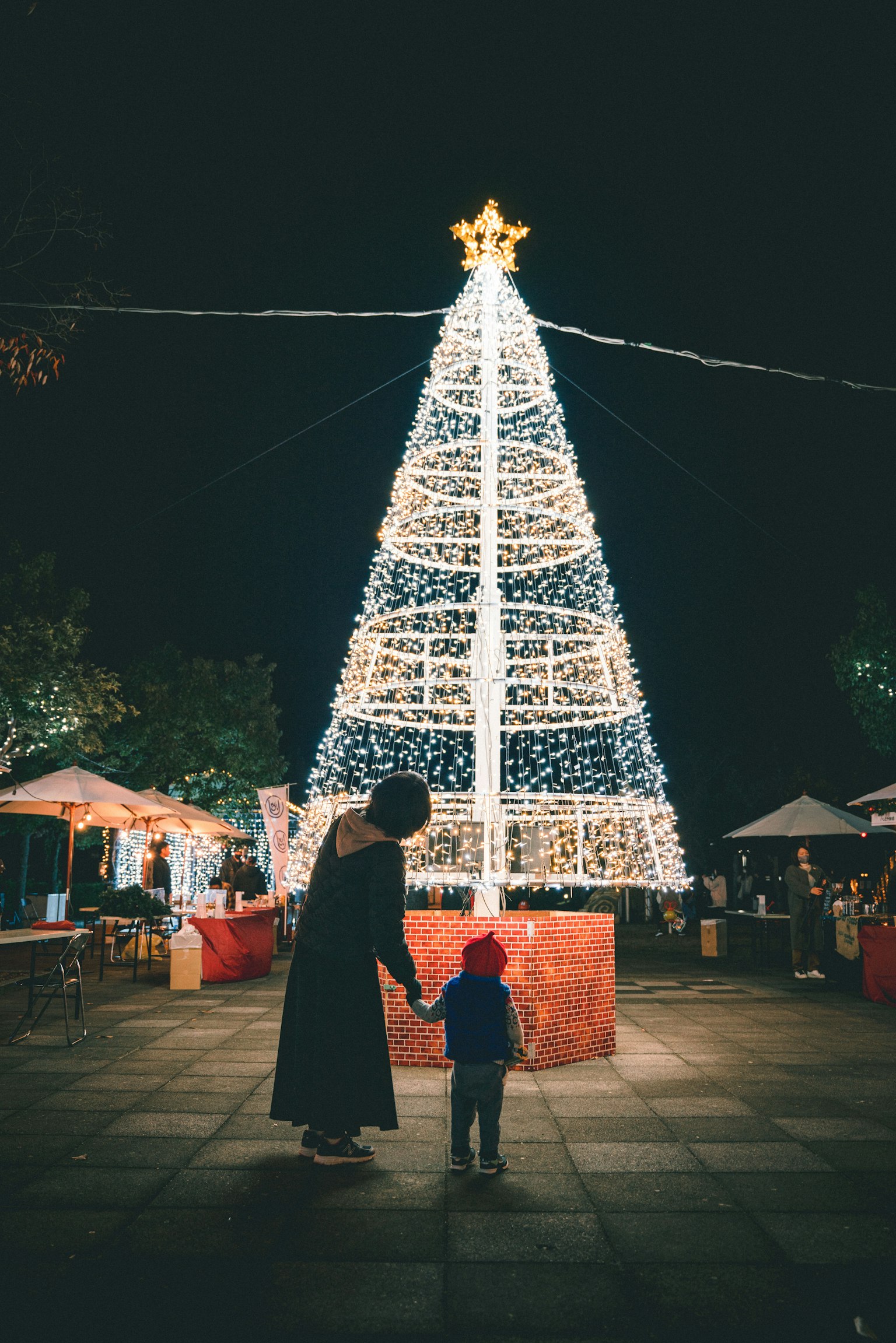 Silhouette eines Elternteils und eines Kindes vor einem beleuchteten Weihnachtsbaum bei Nacht