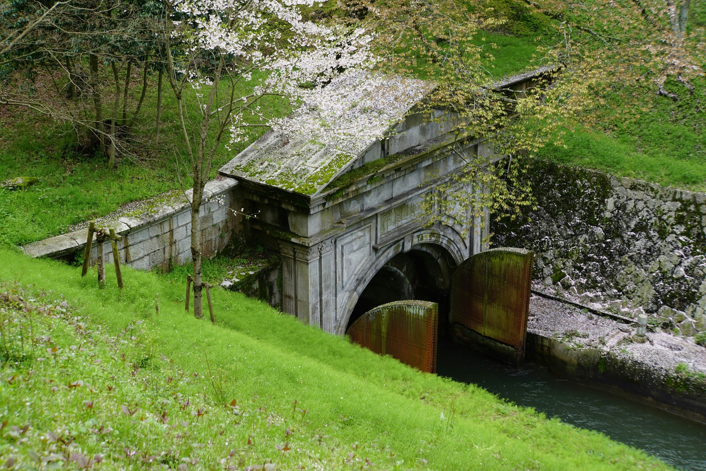 緑の斜面にある石積みの水路とアーチ橋の遺構