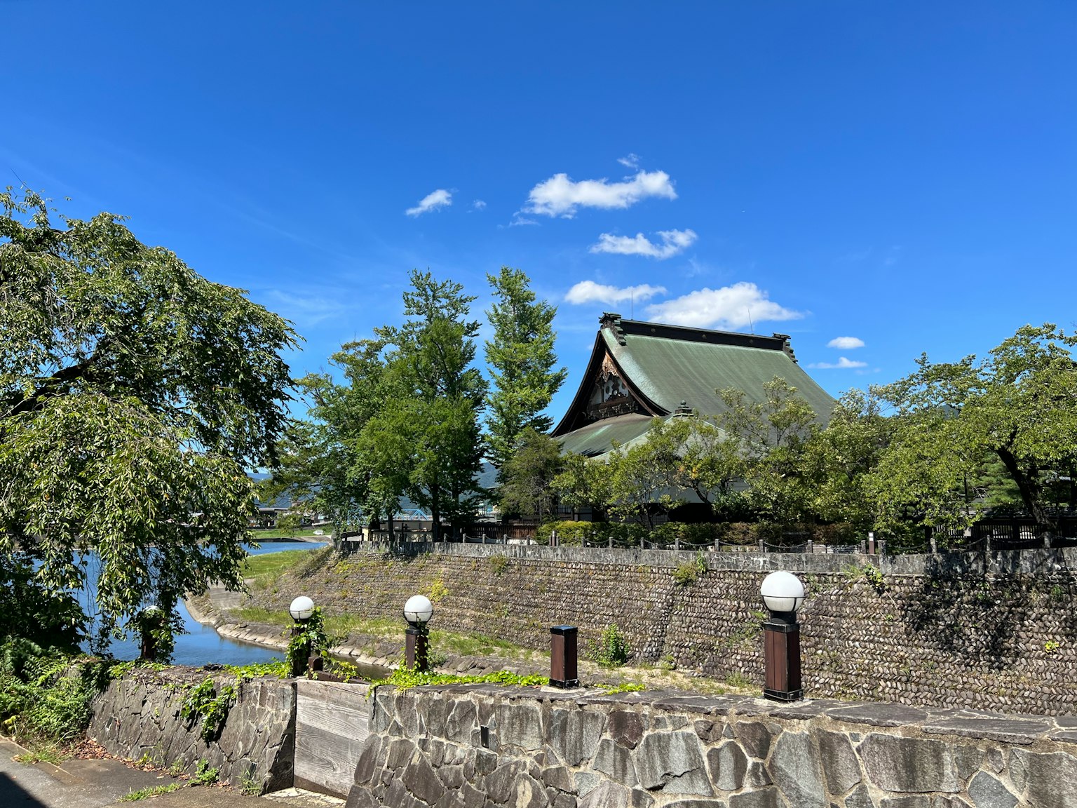 Bangunan tradisional Jepang di bawah langit biru dengan vegetasi dan dinding batu