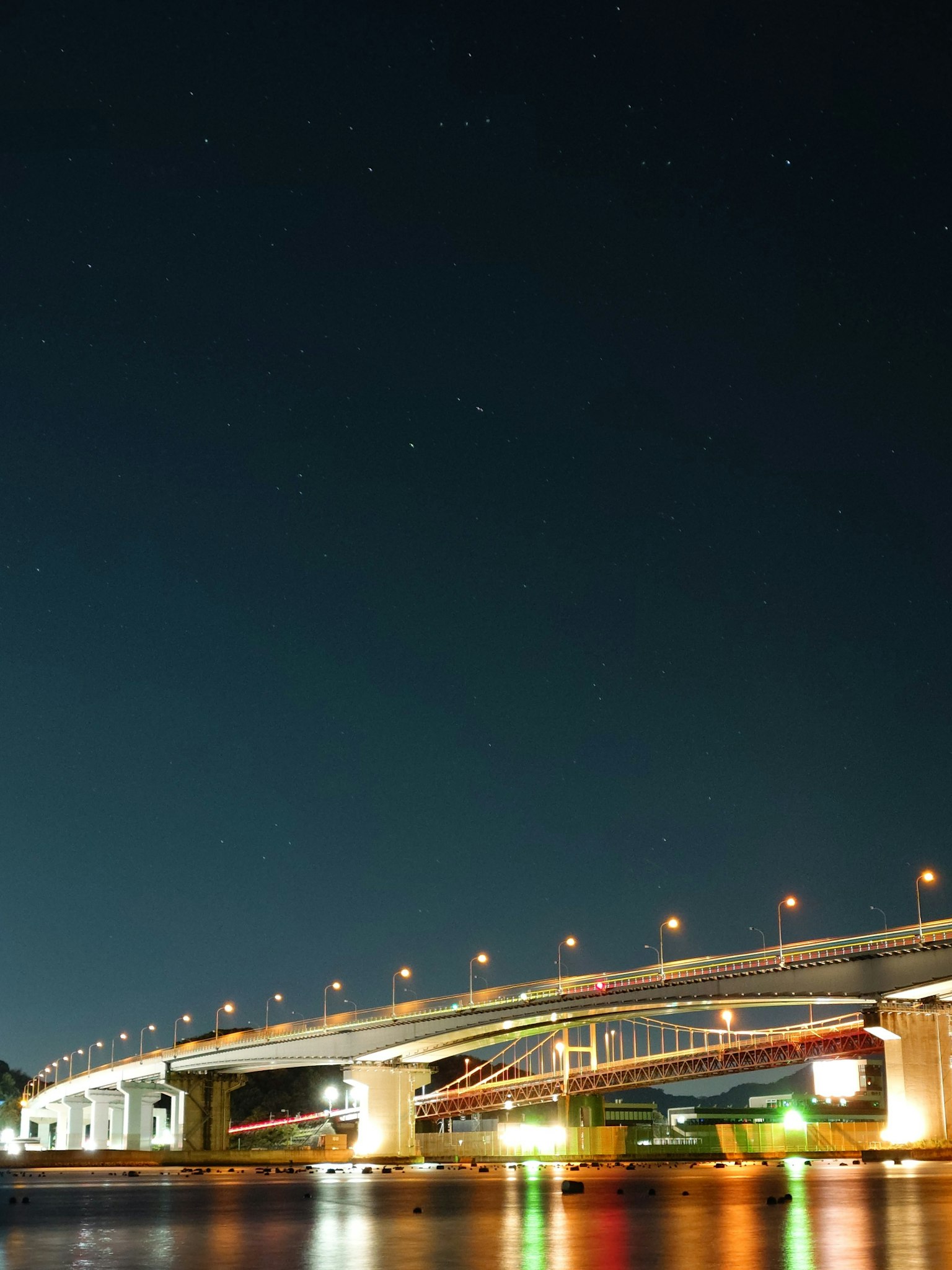 ทิวทัศน์ยามค่ำคืนของสะพานที่สว่างไสวใต้ท้องฟ้าที่เต็มไปด้วยดาว