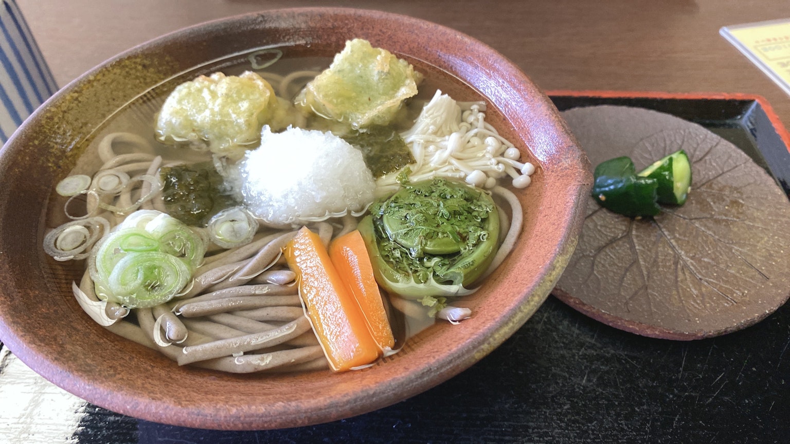 Una ciotola di noodles soba caldi guarnita con tempura, cipolle verdi, daikon grattugiato e verdure