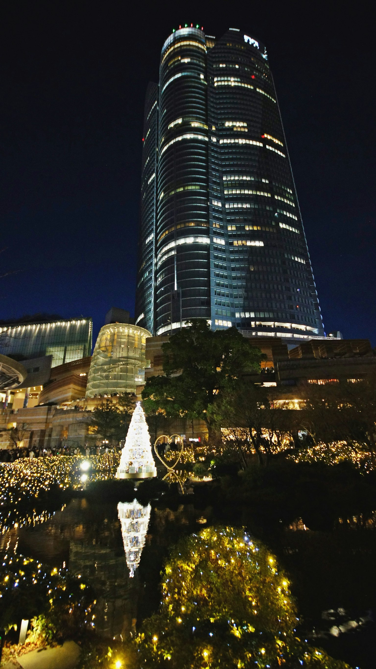 A skyscraper illuminated against the night sky surrounded by festive lights