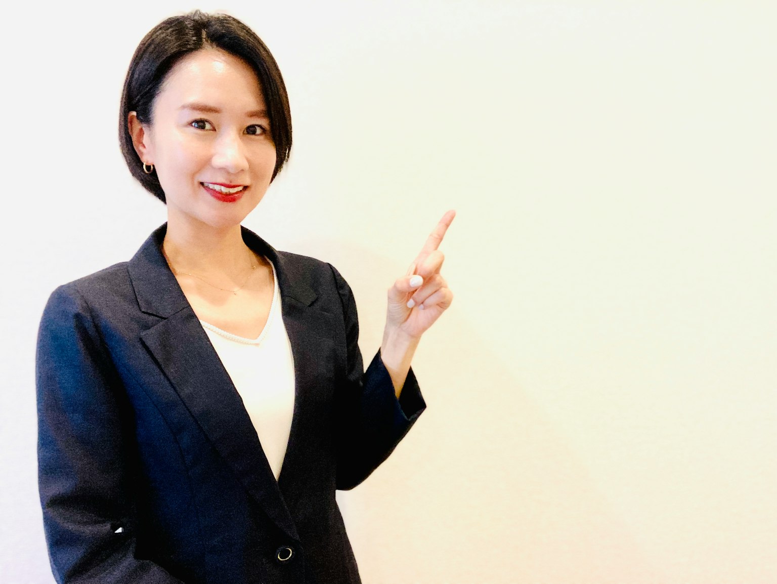 ผู้หญิงในชุดสูทชี้ไปที่พื้นหลังเรียบง่าย