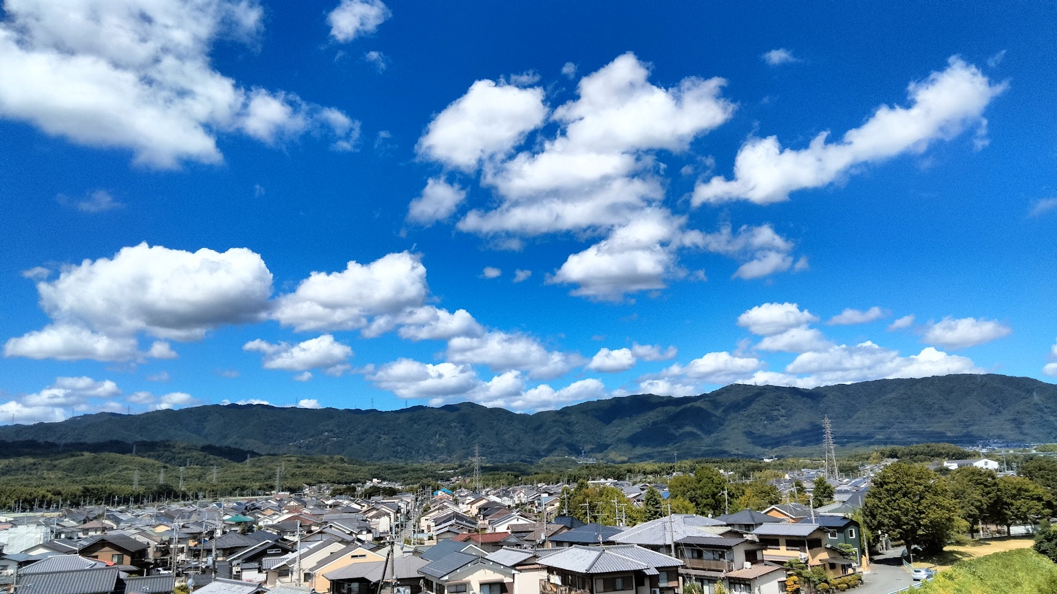 Landschaft mit blauem Himmel und weißen Wolken über einem bergigen Gebiet mit Häusern