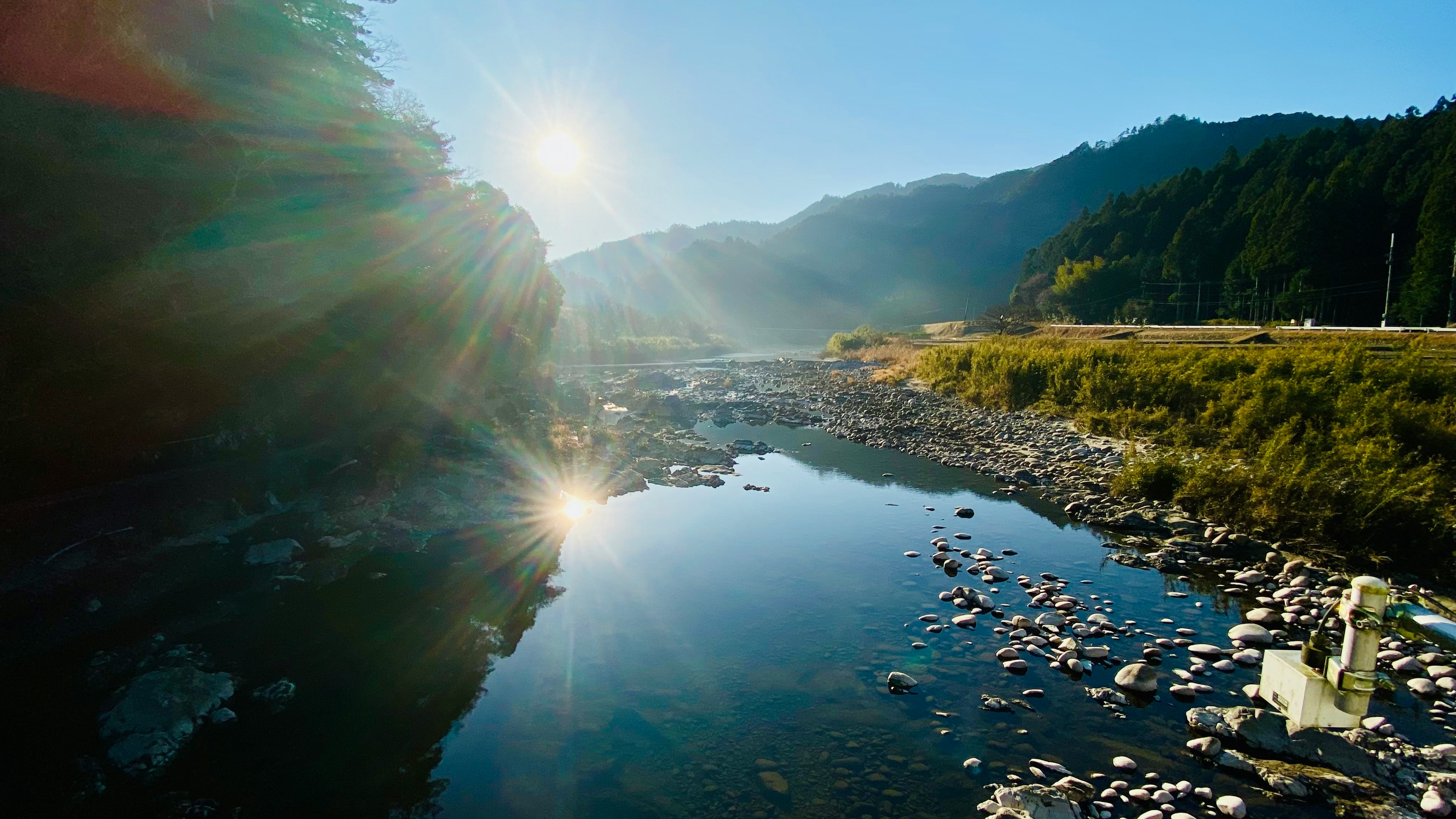 朝日が差し込む川沿いの岩場と山並み
