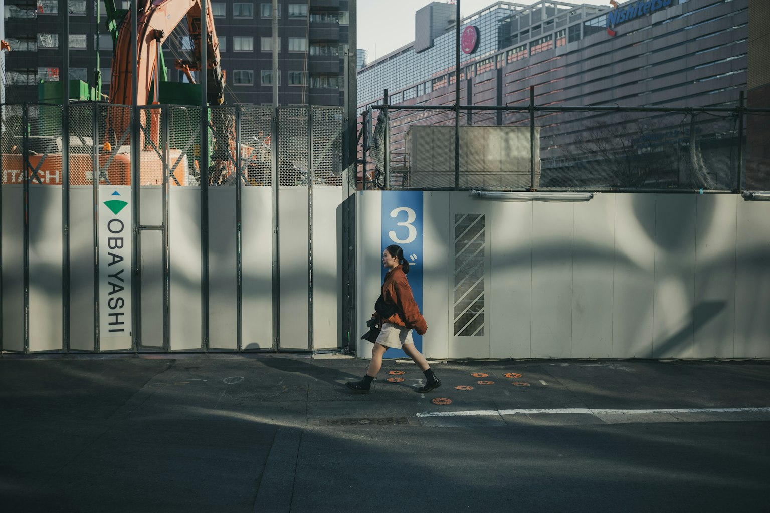 Une personne marchant devant un chantier avec des contrastes de lumière et d'ombre frappants