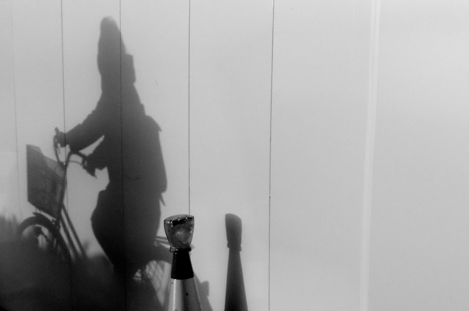 自転車に乗る人の影が白い壁に映るモノクロの画像
