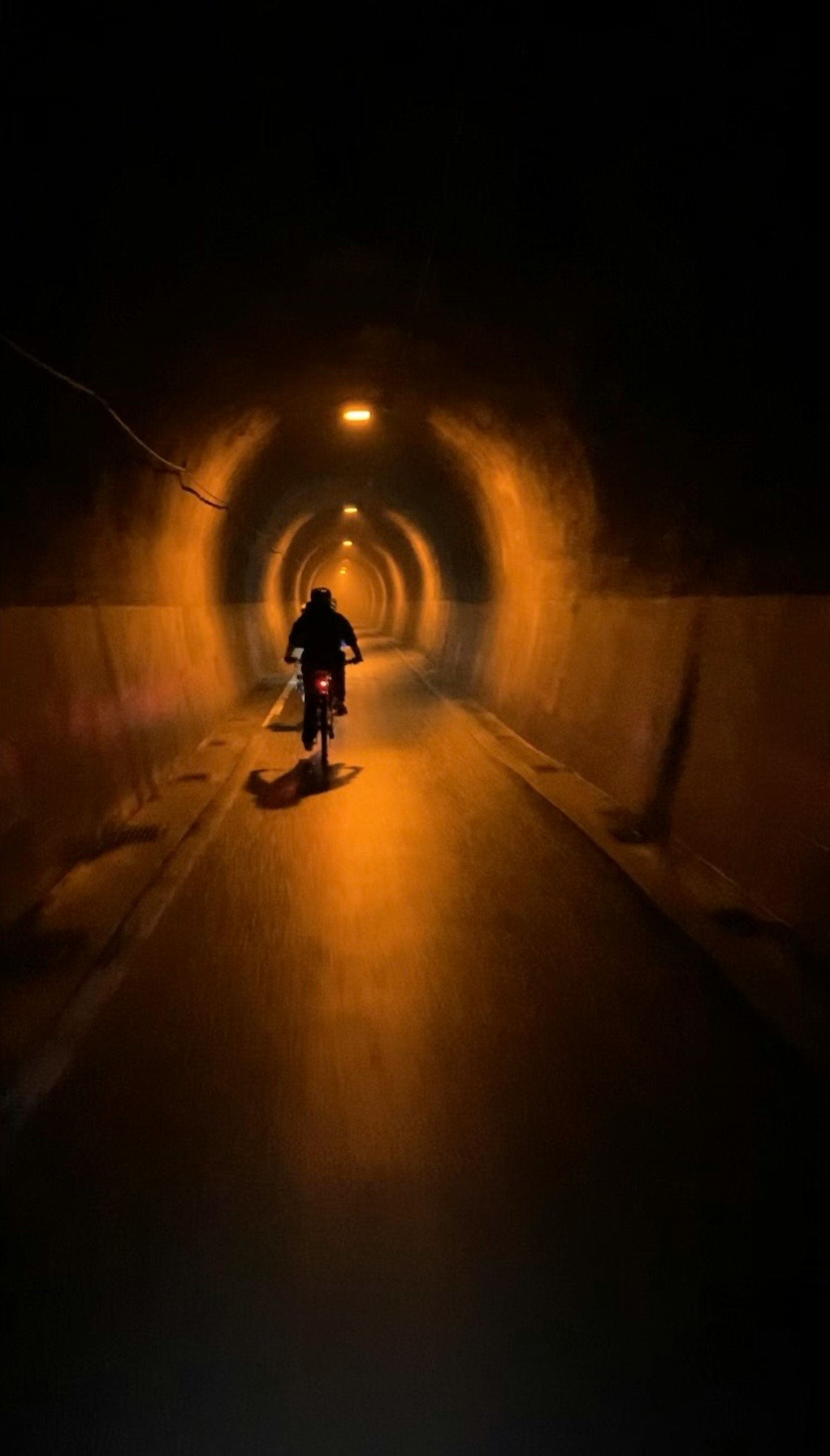 Silhouette of a person riding a bicycle through a dark tunnel