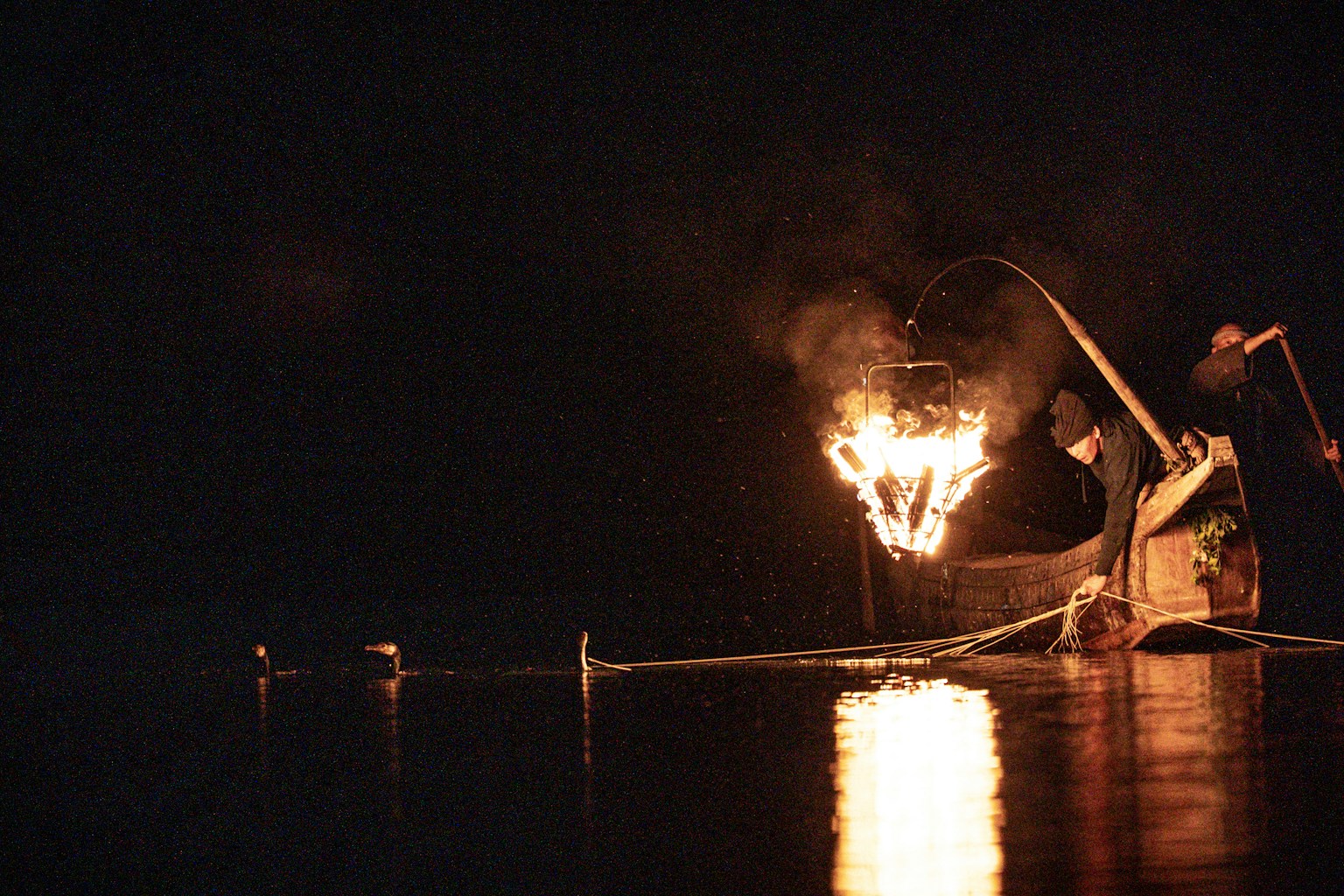 Fisherman using fire to fish on a dark water surface