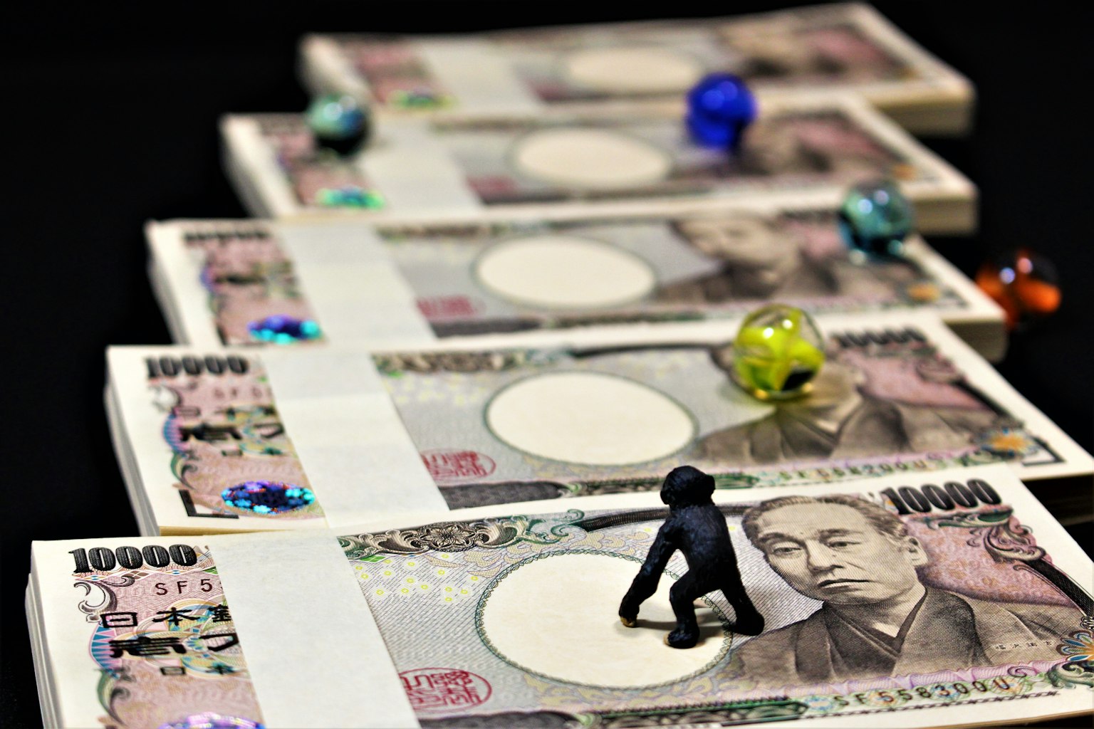 A stack of Japanese yen bills with a miniature figure and colorful marbles on top