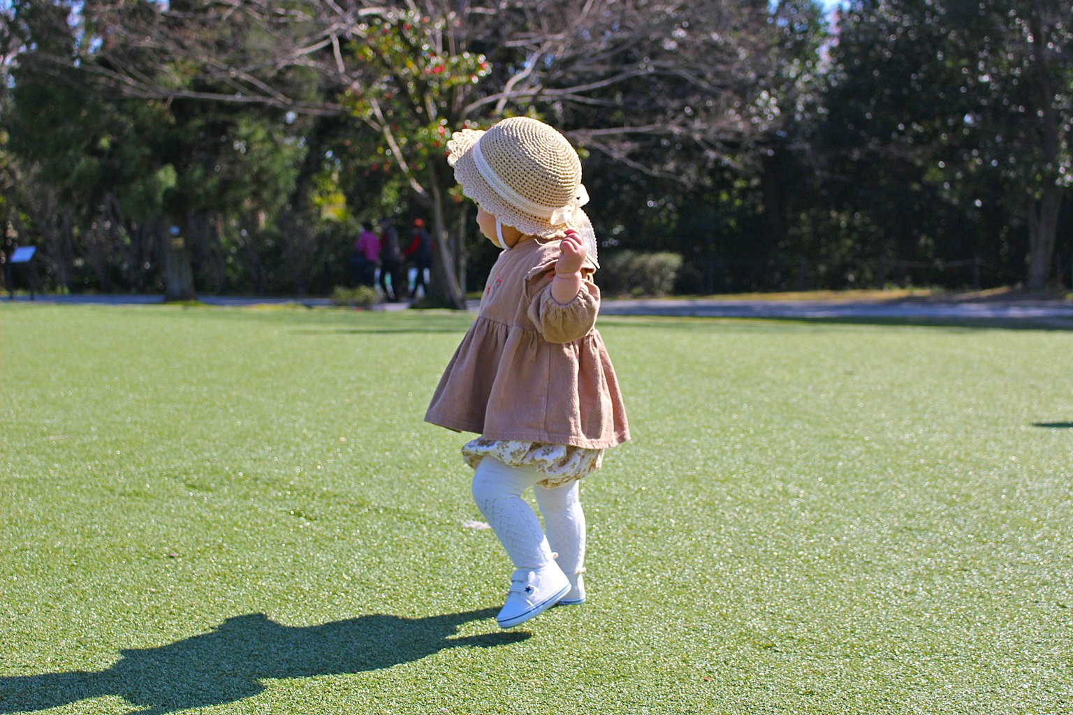 Ein Kind, das auf dem Gras spielt, trägt ein sanft gefärbtes Kleid und einen Hut