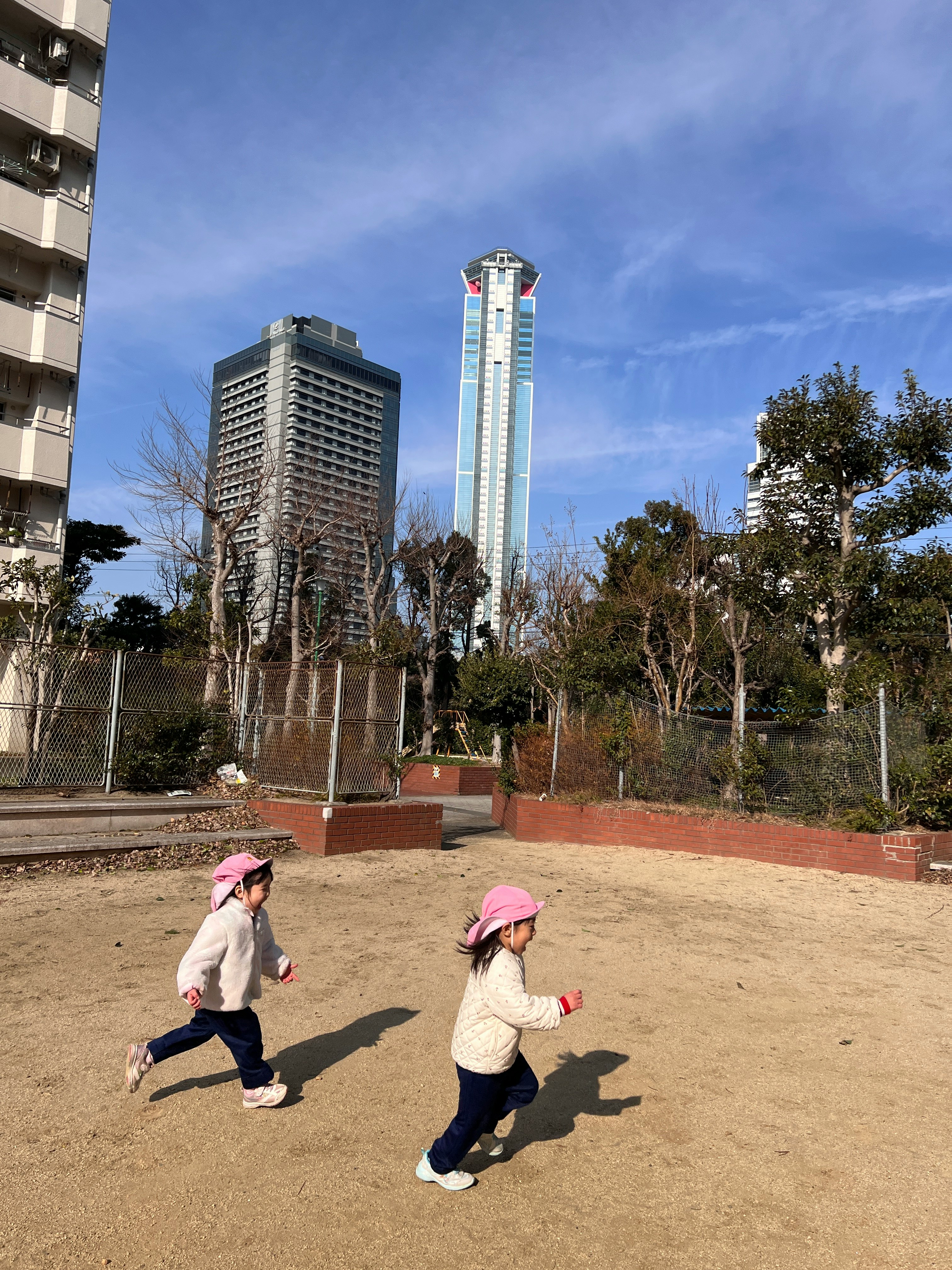 青空の下で走る子どもたちと高層ビルが見える公園