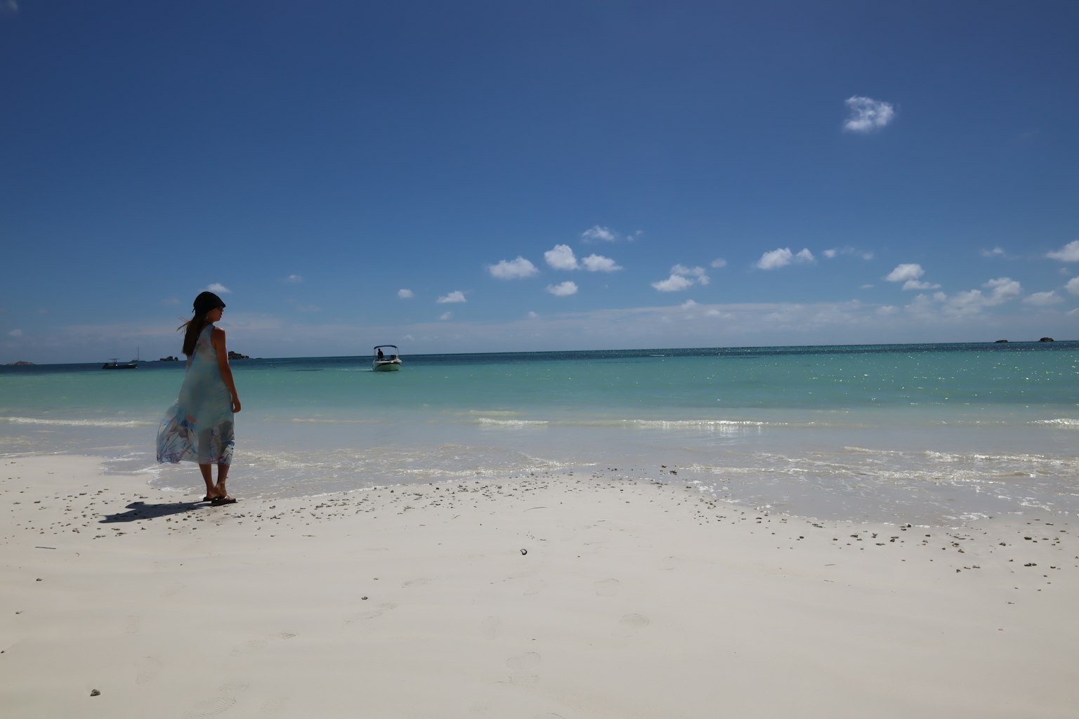 Une femme se tenant sur une plage de sable blanc avec une mer bleue et un ciel dégagé