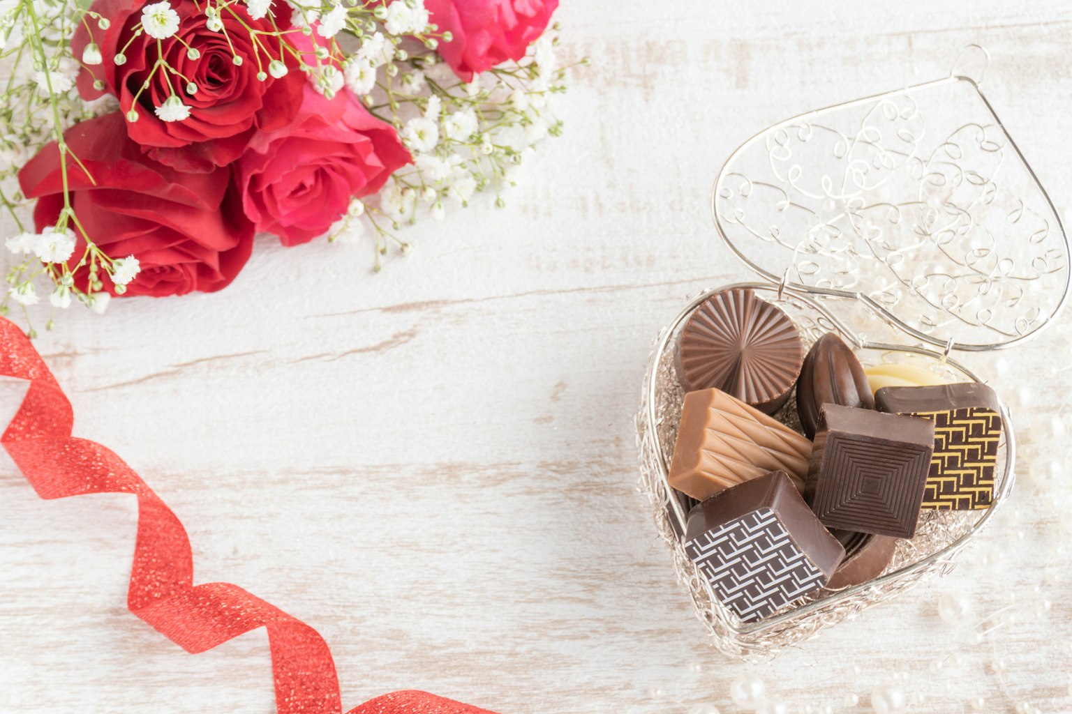Caja en forma de corazón llena de chocolates surtidos y un ramo de rosas rojas