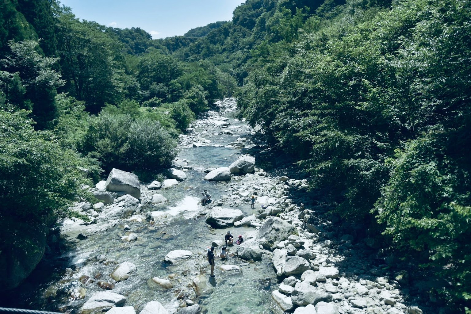 Un fiume sereno che scorre tra montagne verdi lussureggianti con rocce sparse e due persone che si dedicano ad attività a riva