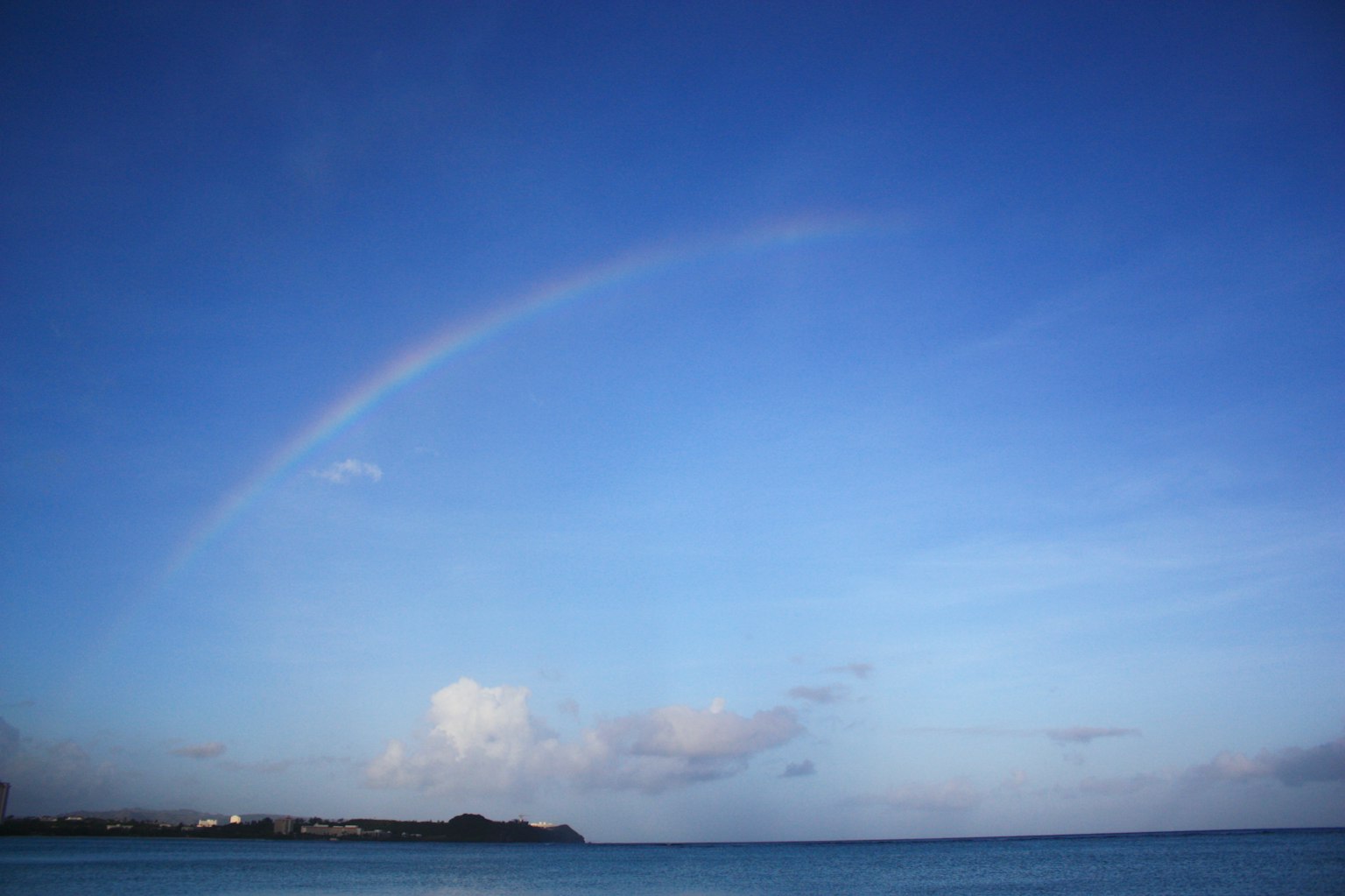 A rainbow arching across a blue sky over the ocean