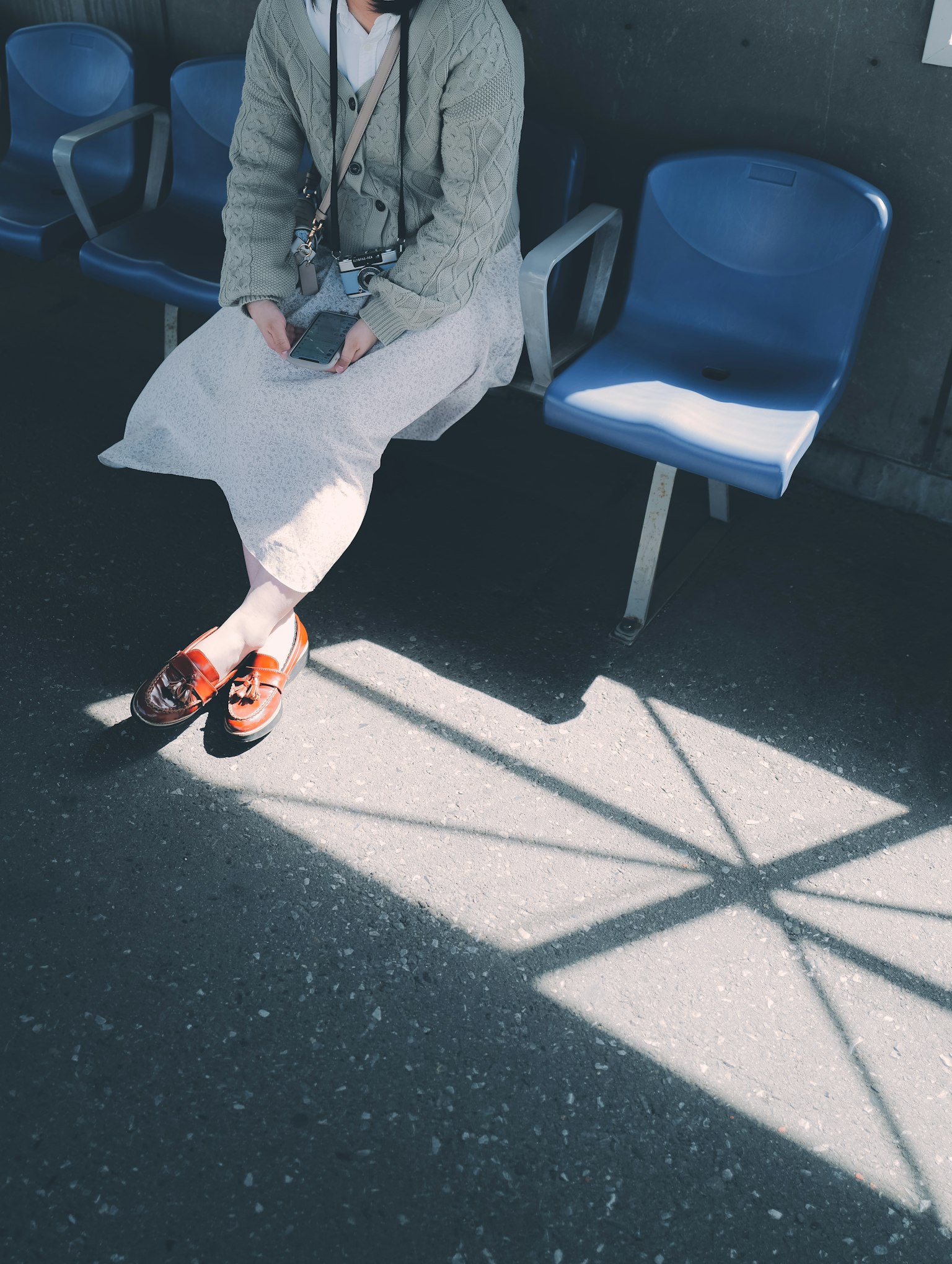 Woman sitting with brown shoes on blue chairs casting shadows