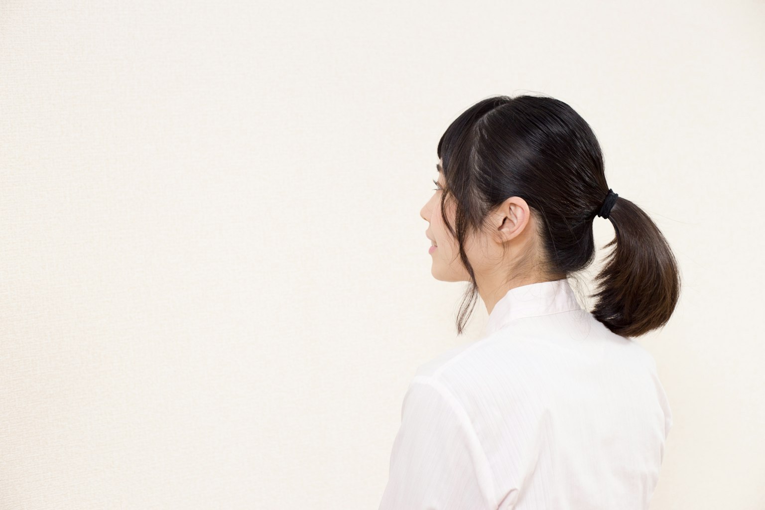Seorang wanita yang menghadap ke belakang mengenakan kemeja putih dengan rambut diikat kuncir kuda