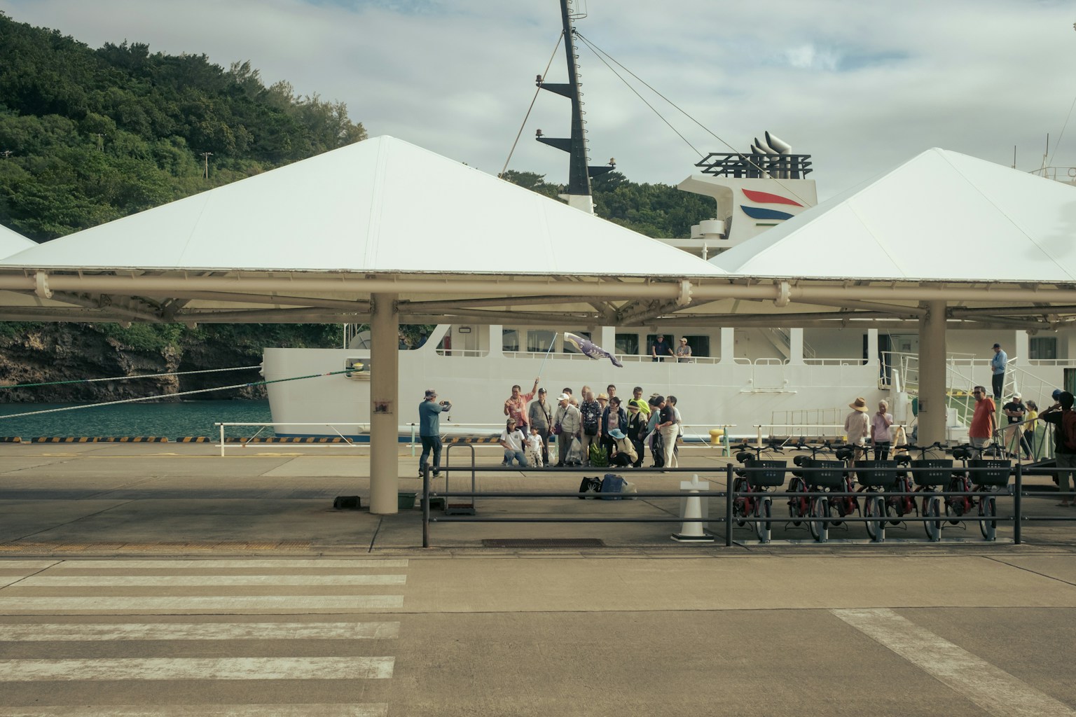 白いテントの下に集まる人々と船が見える港の風景