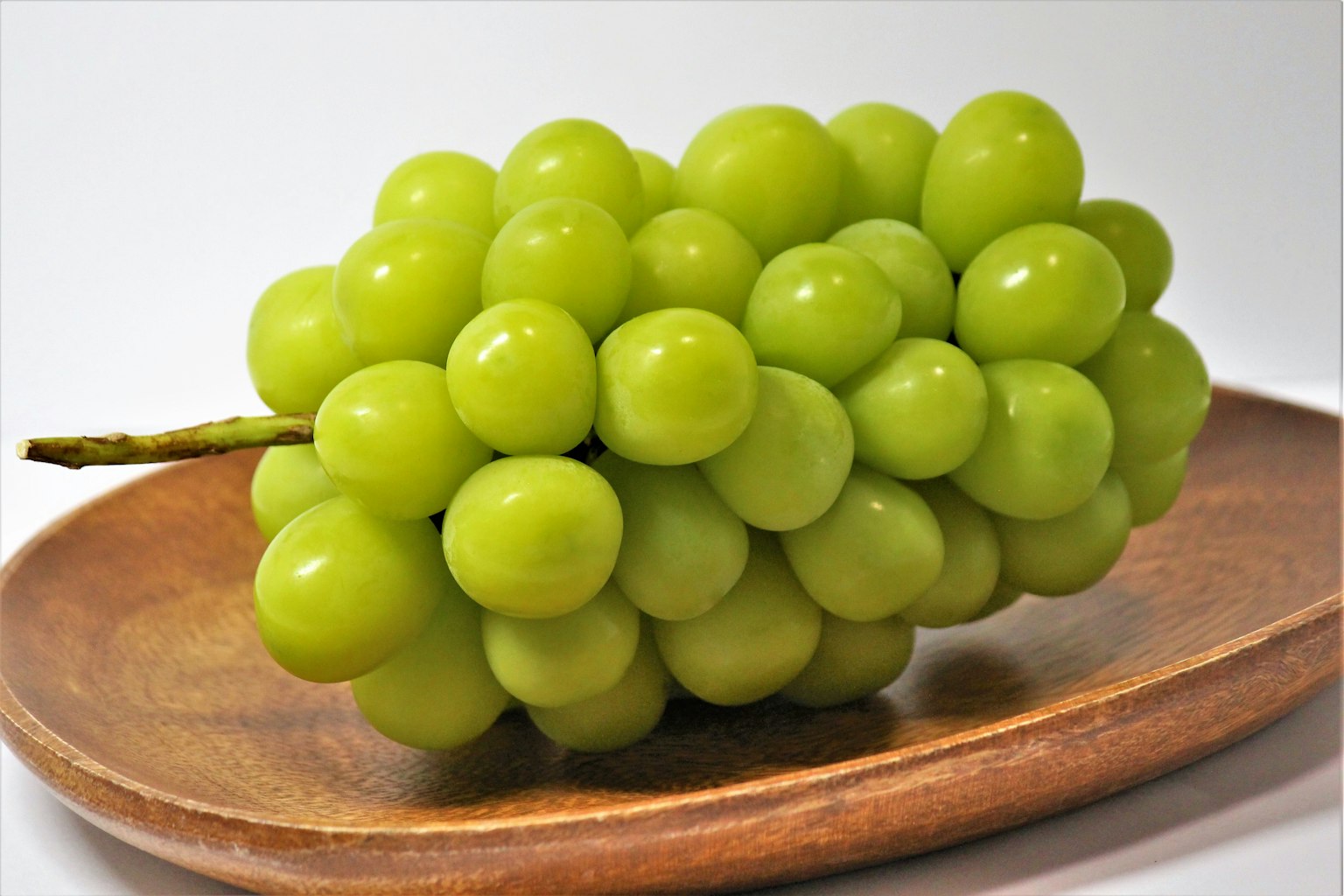 A cluster of green grapes resting on a wooden plate