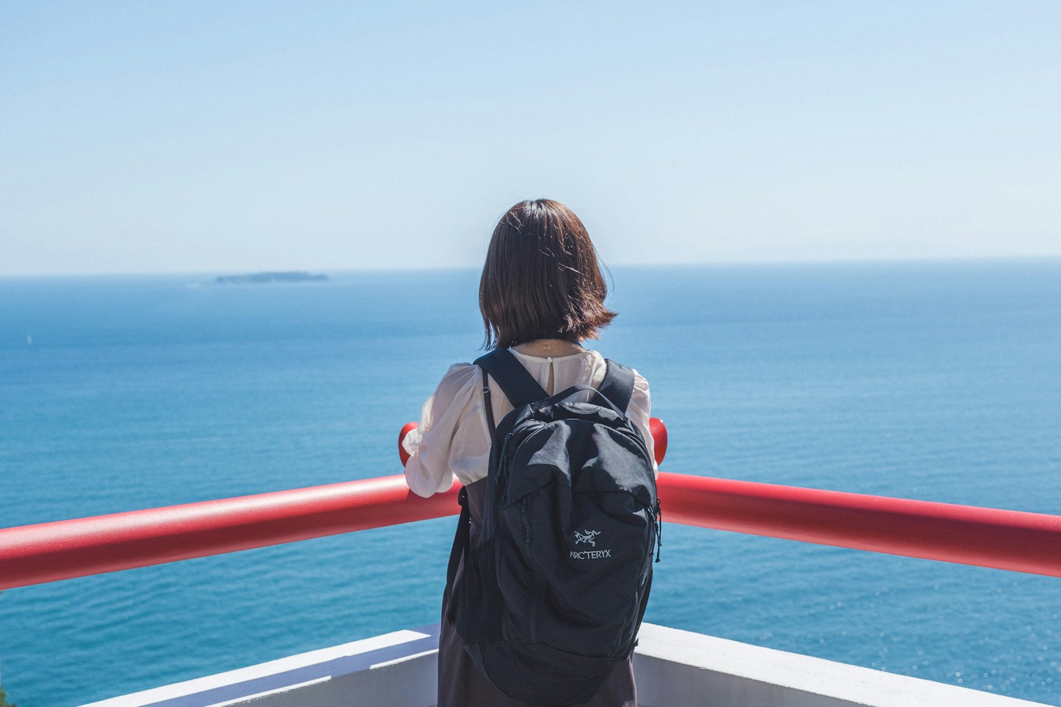 Woman gazing at the blue sea with a red railing