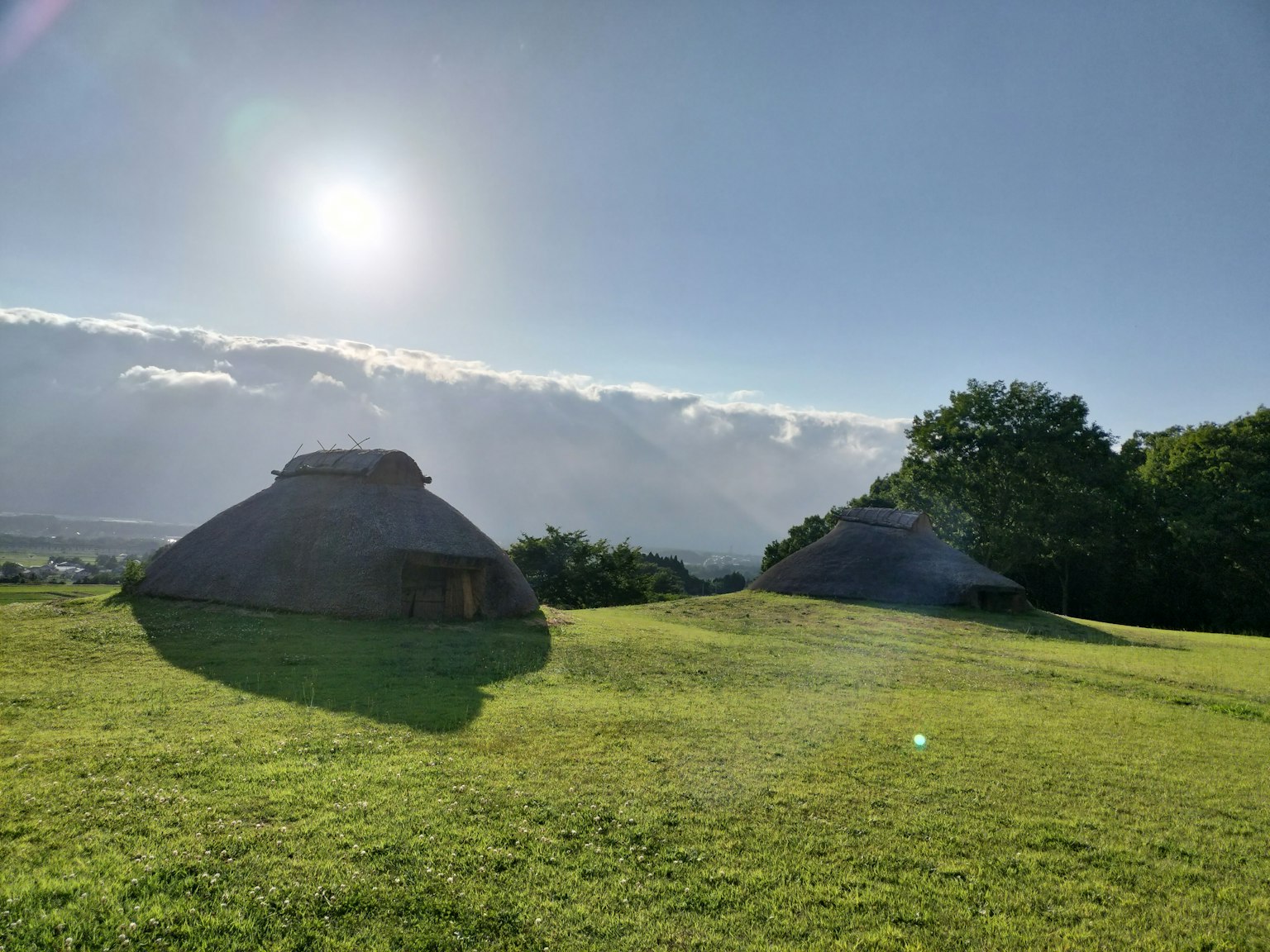 Two traditional round-roof houses on a grassy field with a bright sun