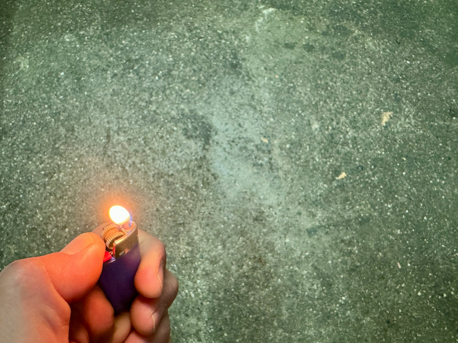 一只手握着点燃的蓝色打火机在纹理地面上方