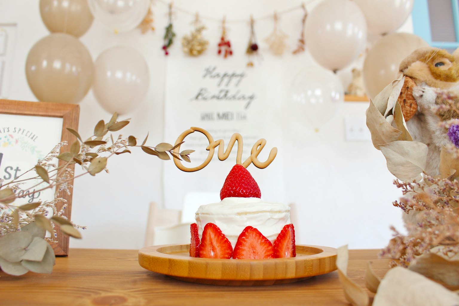 Un gâteau d'anniversaire décoré de fraises pour une célébration d'un an avec des ballons en arrière-plan