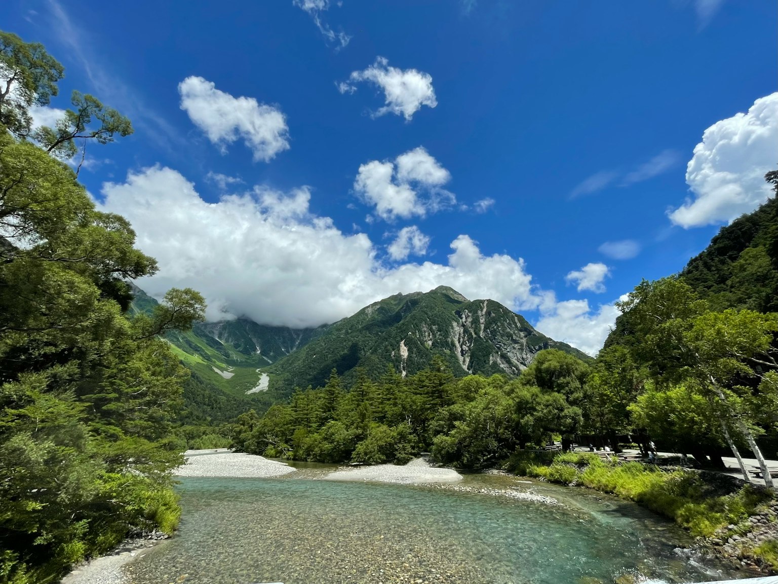 藍天和白雲下的山脈與河流的美麗景色，周圍被郁郁蔥蔥的綠樹環繞