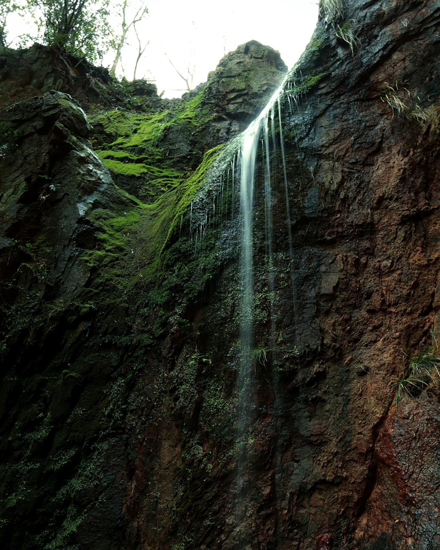Pemandangan indah air terjun yang mengalir di dinding batu yang ditutupi lumut