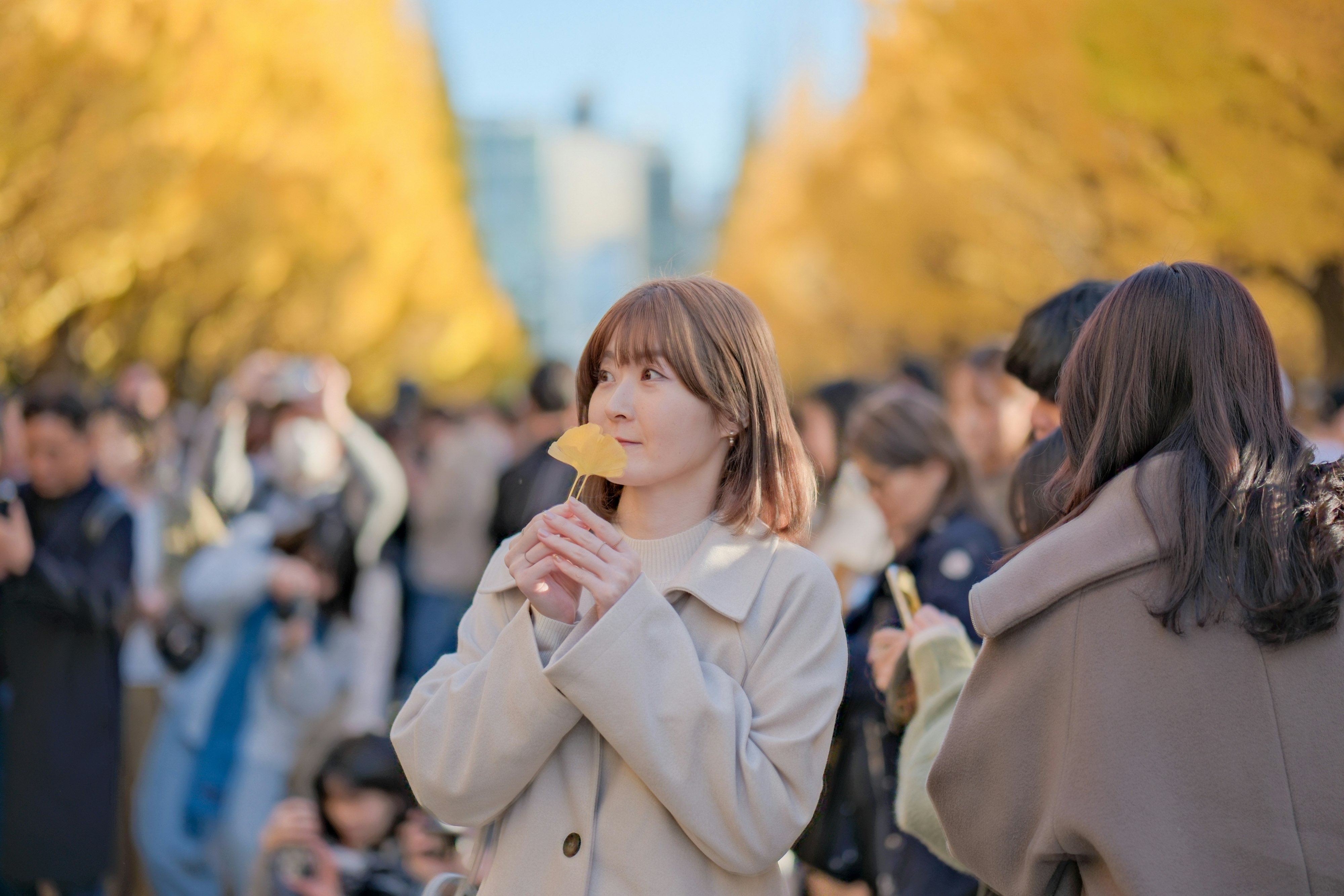 秋の並木道で飲み物を手にする女性たちの街角風景