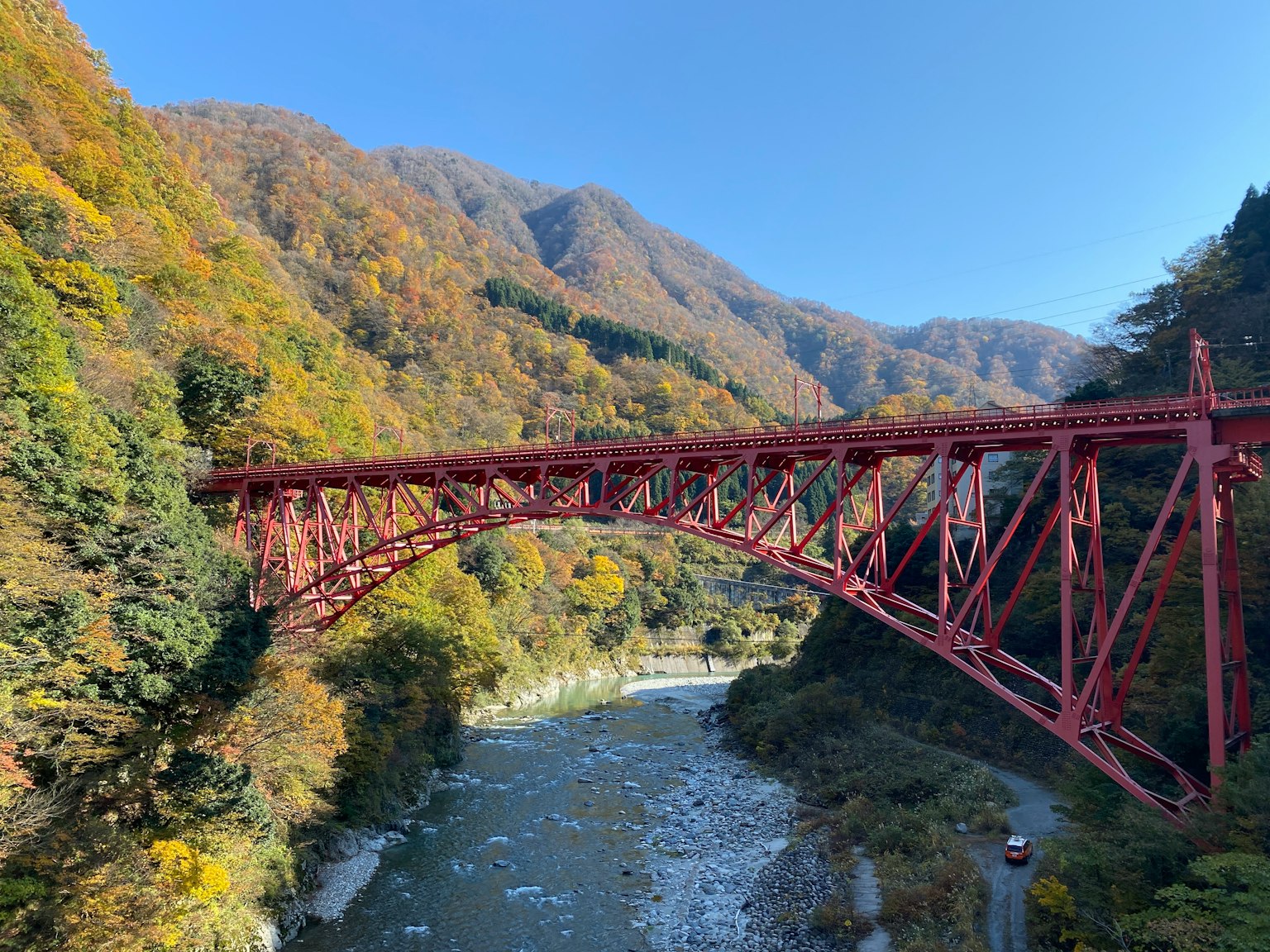 Un puente rojo que cruza un río con follaje otoñal en las montañas