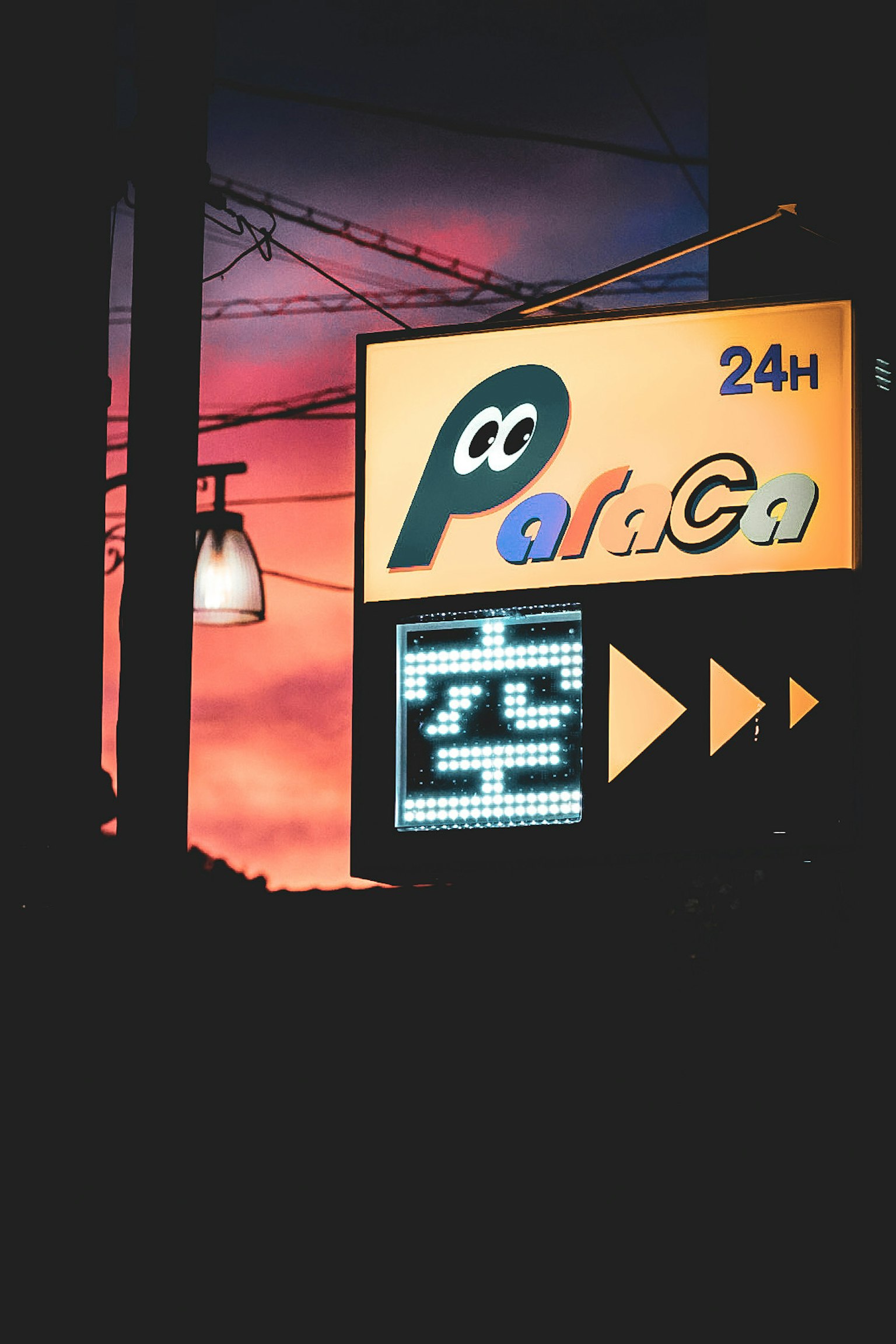 24-Stunden-Schild mit buntem Hintergrund und Straßenlaterne bei Sonnenuntergang