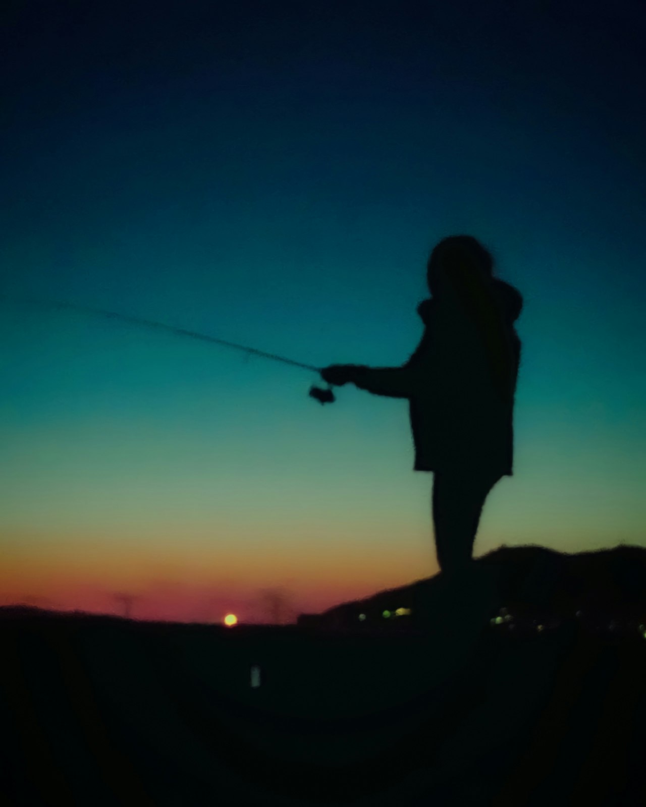 マジックアワーの海辺で釣りをする人と夕焼けの空