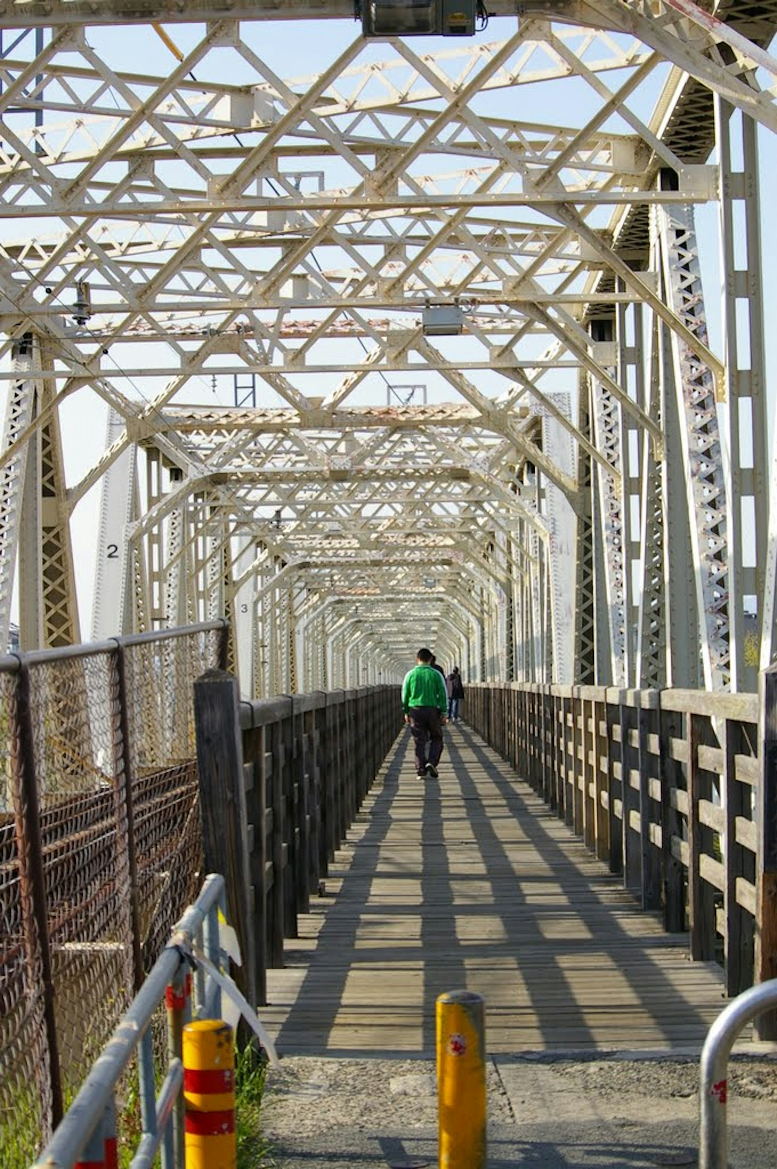Person walking on a metal bridge with intricate patterns and shadows